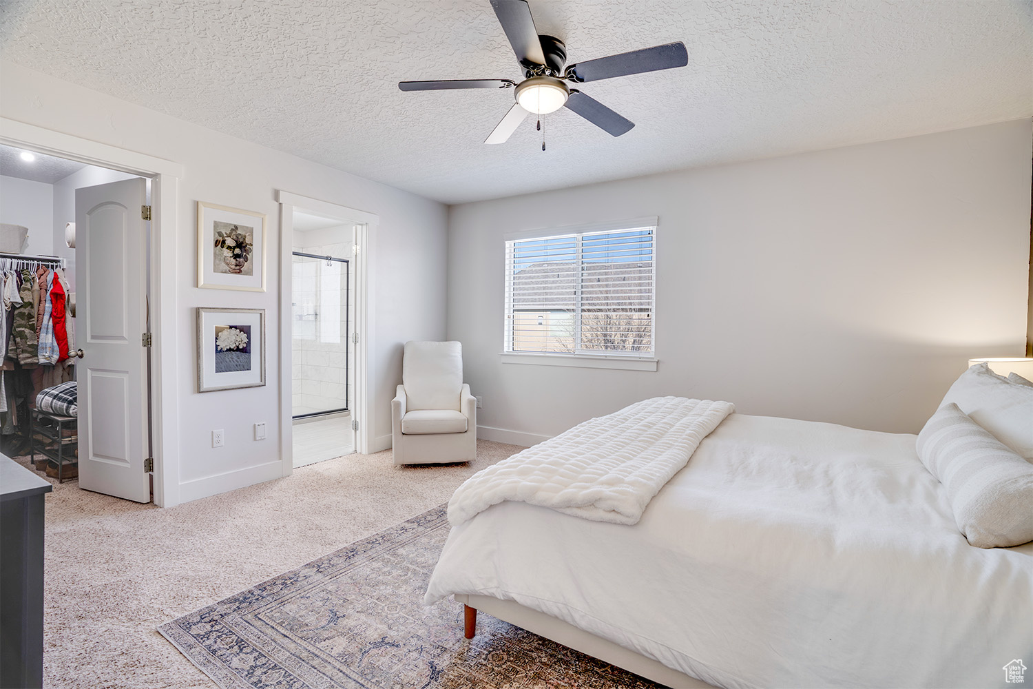 Bedroom featuring a spacious closet, light colored carpet, a textured ceiling, ensuite bath, and a closet