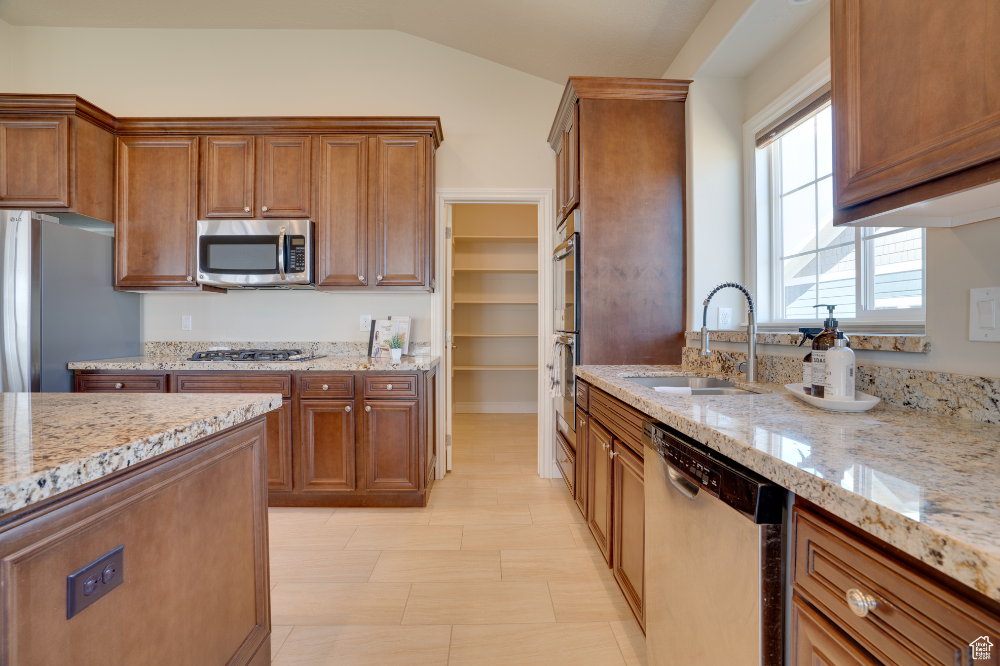 Kitchen with sink, vaulted ceiling, light stone countertops, and appliances with stainless steel finishes