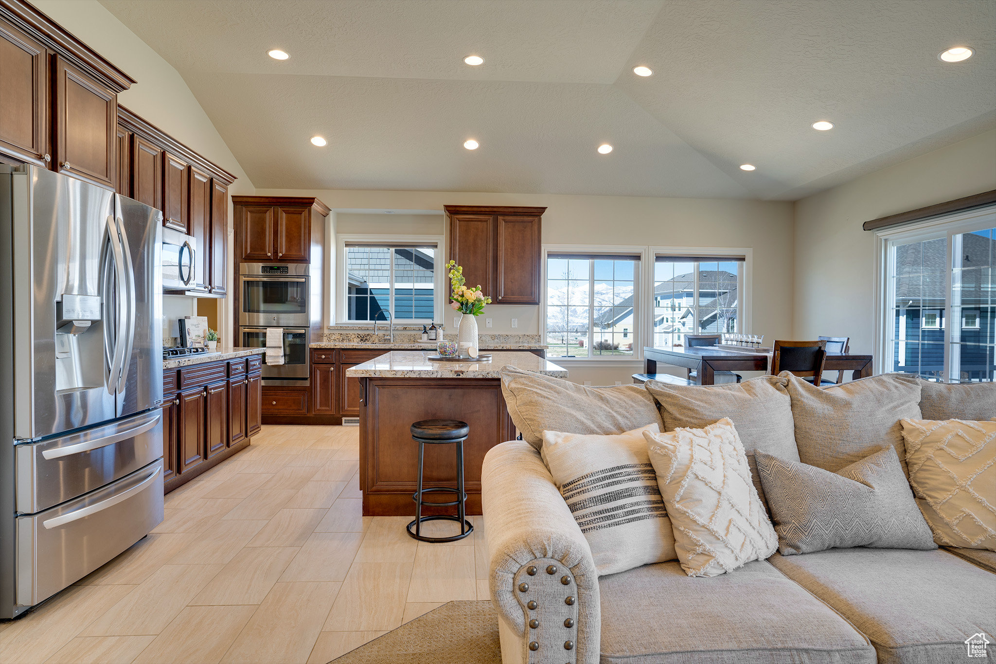 Kitchen with a breakfast bar, a center island, vaulted ceiling, stainless steel appliances, and light stone countertops