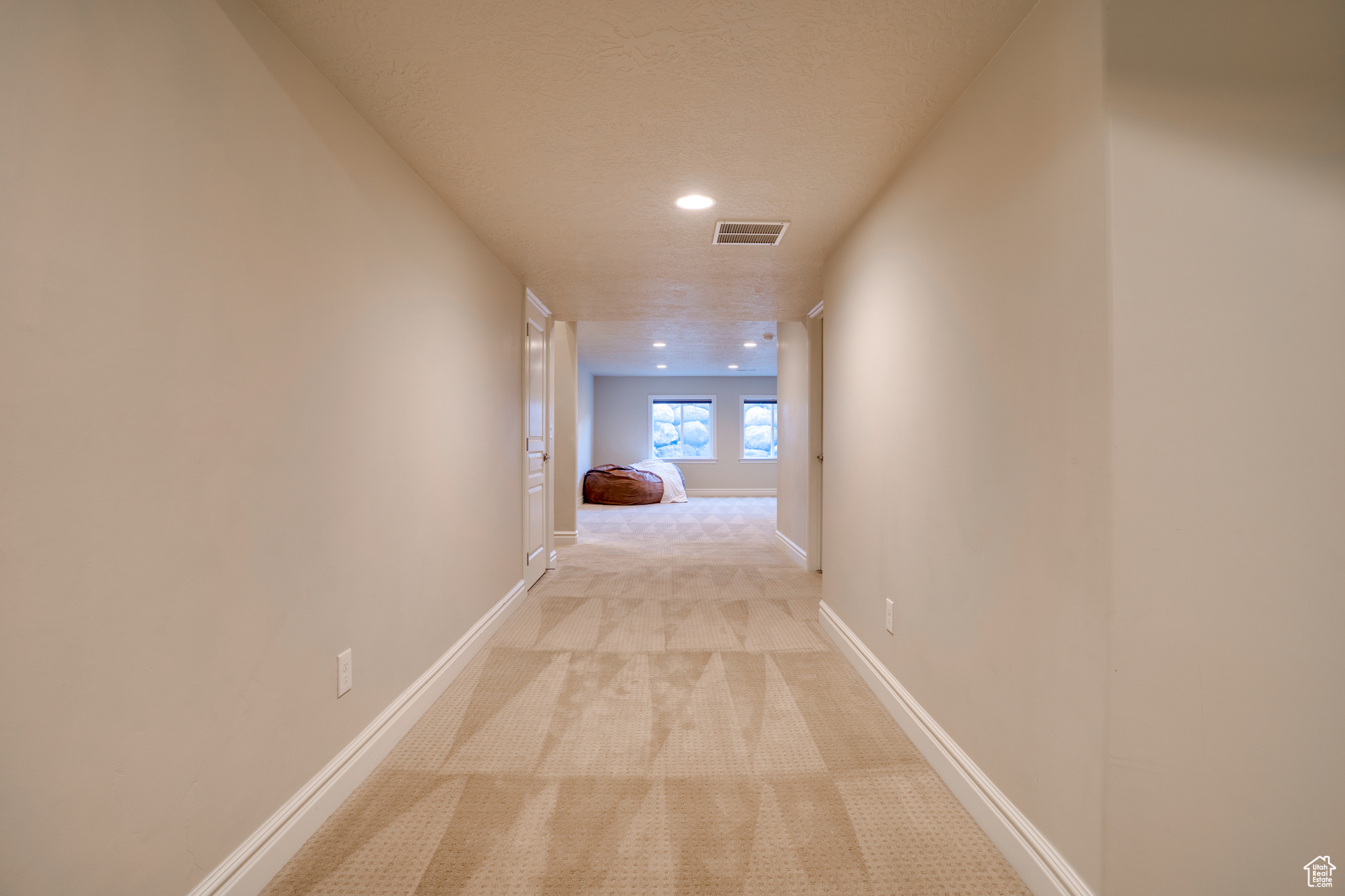 Corridor featuring light colored carpet and a textured ceiling