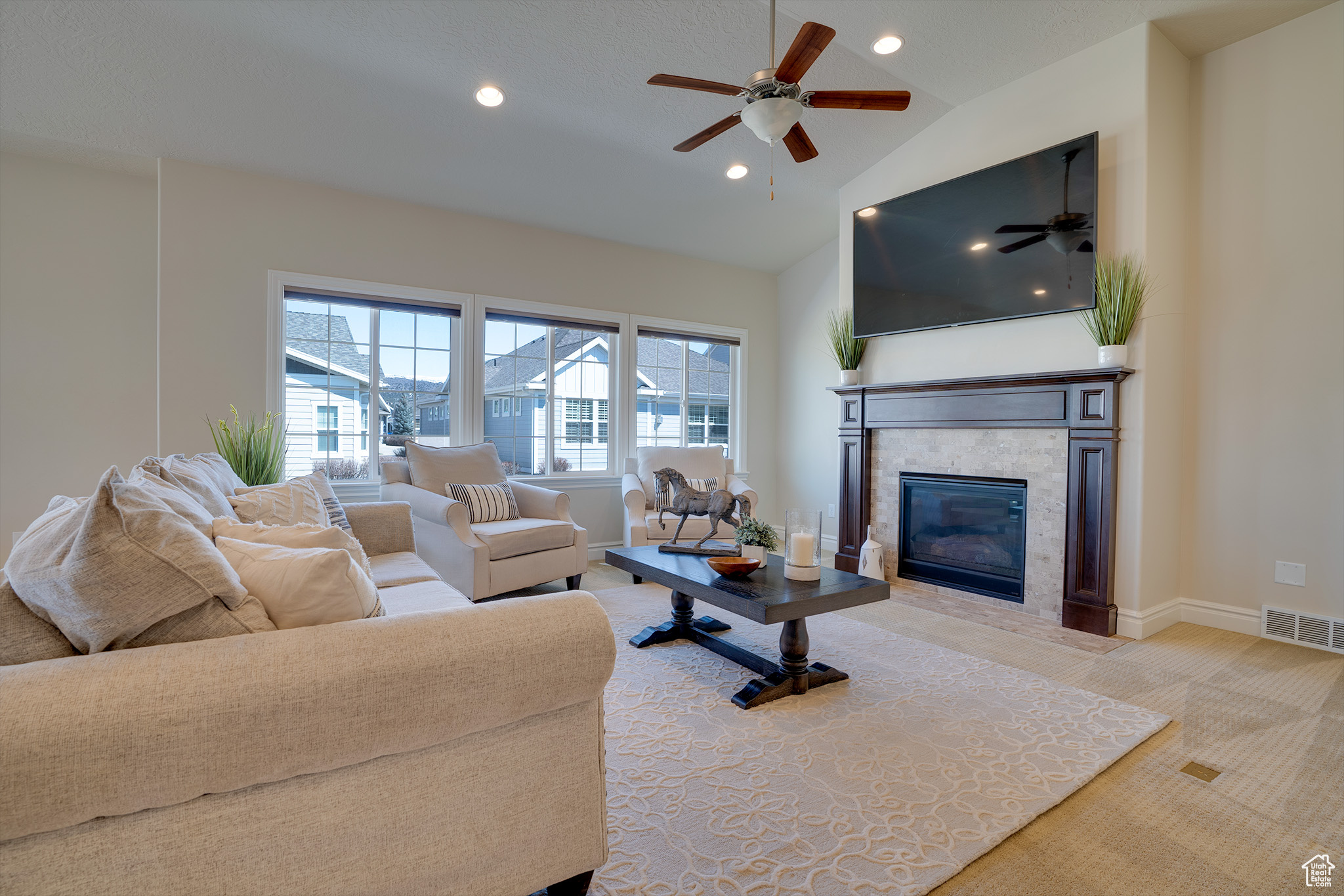 Carpeted living room with ceiling fan, lofted ceiling, and a fireplace