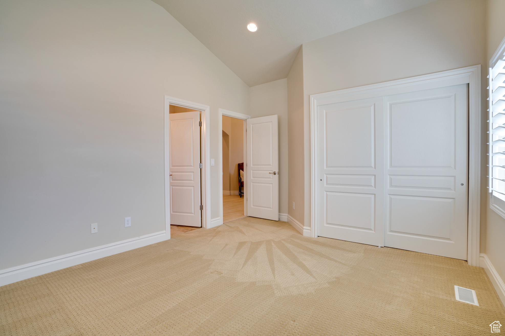 Unfurnished bedroom with light colored carpet, high vaulted ceiling, and a closet