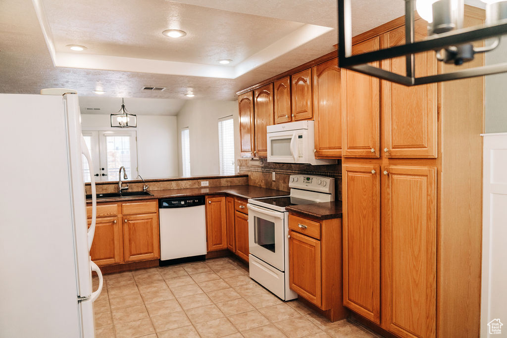 Kitchen featuring sink, white appliances, hanging light fixtures, light tile patterned flooring, and a raised ceiling