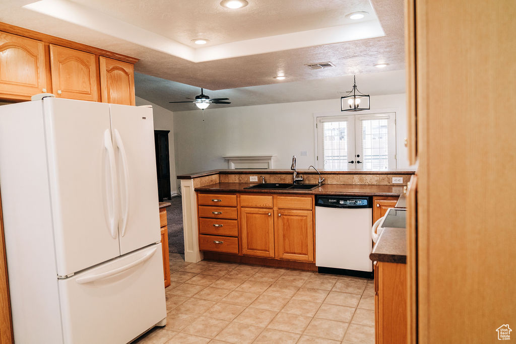 Kitchen featuring a raised ceiling, sink, white appliances, and decorative light fixtures