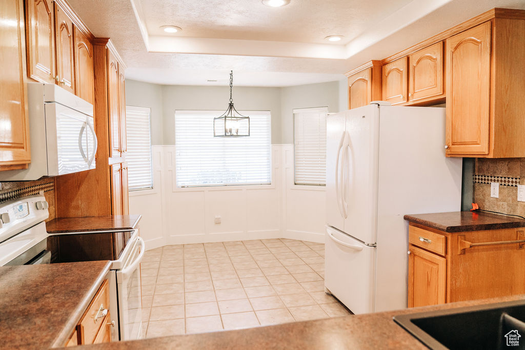 Kitchen featuring decorative light fixtures, light tile patterned floors, a raised ceiling, white appliances, and decorative backsplash