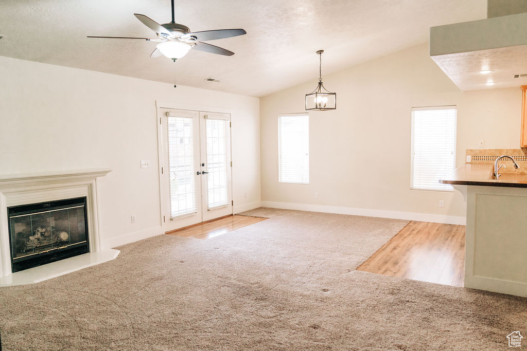 Unfurnished living room with french doors, sink, vaulted ceiling, light carpet, and a textured ceiling