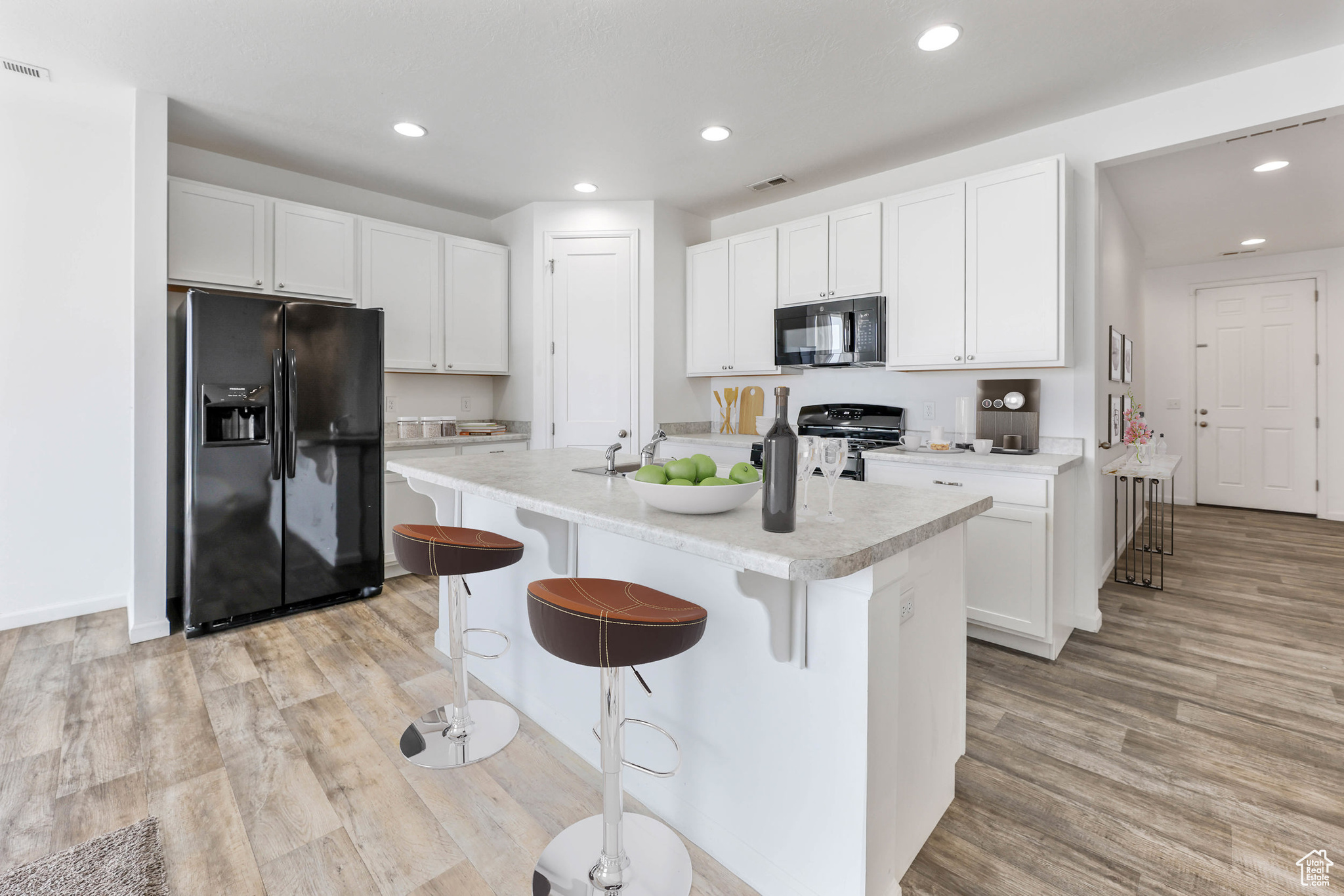 Kitchen with white cabinetry, an island with sink, a kitchen bar, light hardwood / wood-style floors, and black appliances