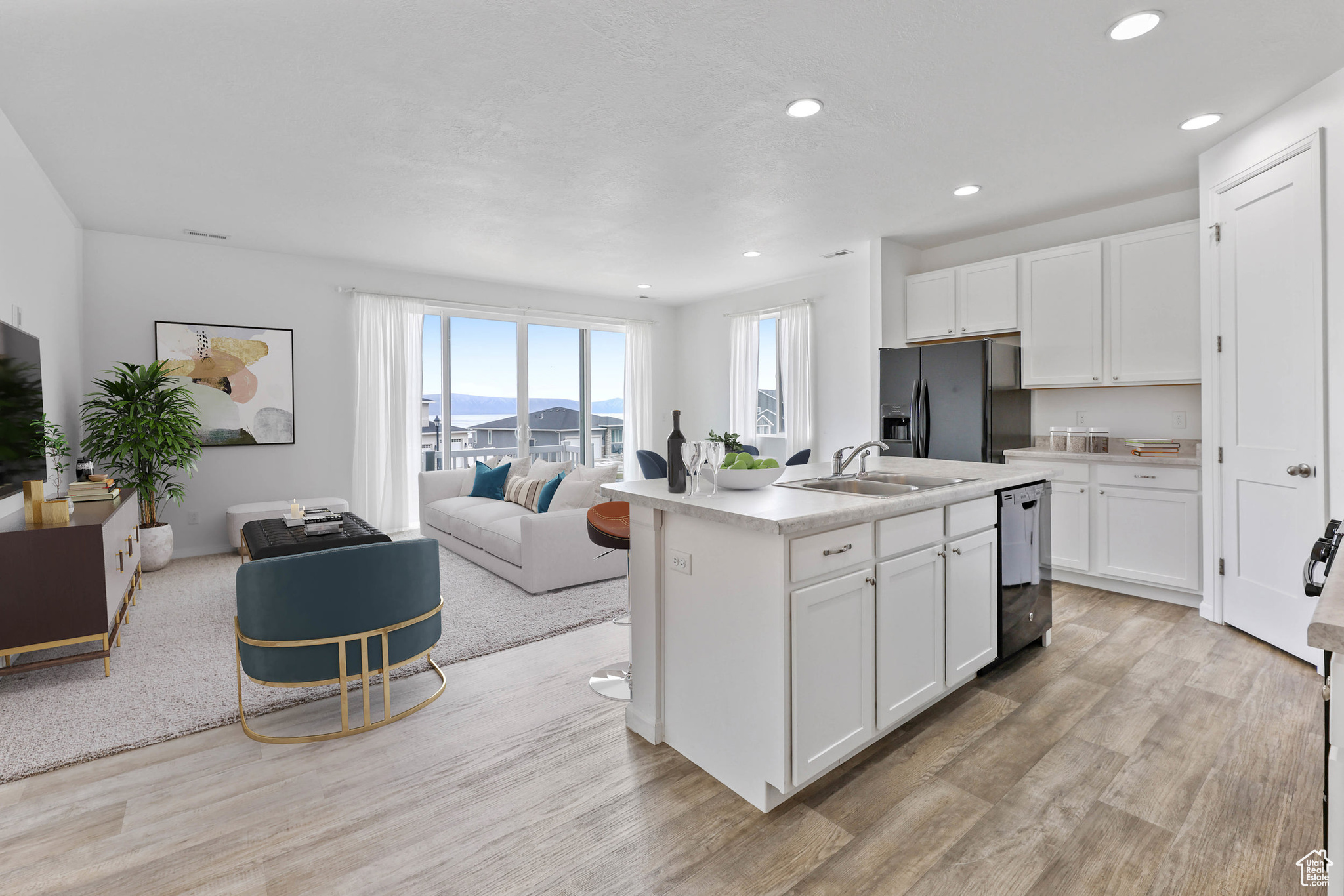 Kitchen with sink, white cabinets, a center island with sink, black fridge with ice dispenser, and light wood-type flooring