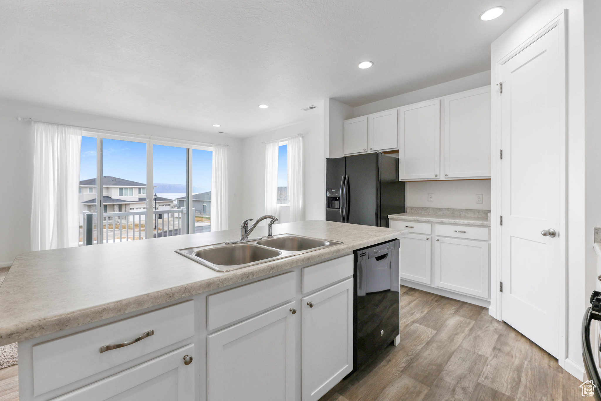 Kitchen with sink, white cabinets, a kitchen island with sink, black appliances, and light hardwood / wood-style flooring