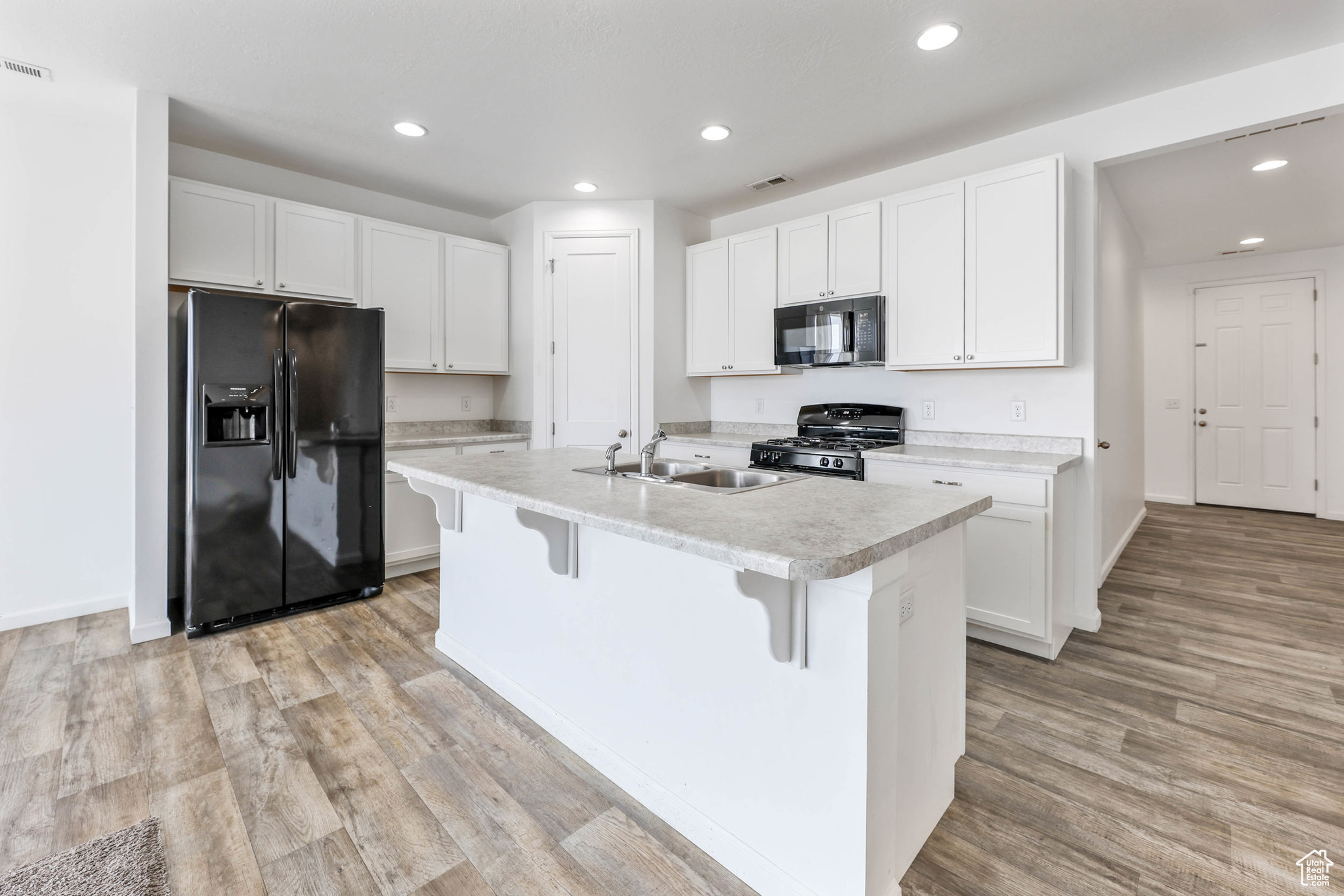 Kitchen featuring white cabinets, sink, a center island with sink, and black appliances