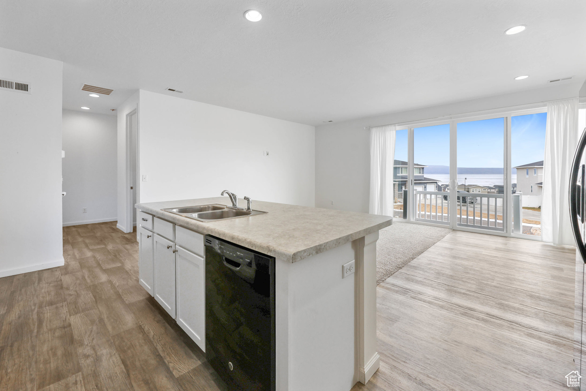 Kitchen with a water view, light hardwood / wood-style flooring, a center island with sink, black dishwasher, and white cabinets