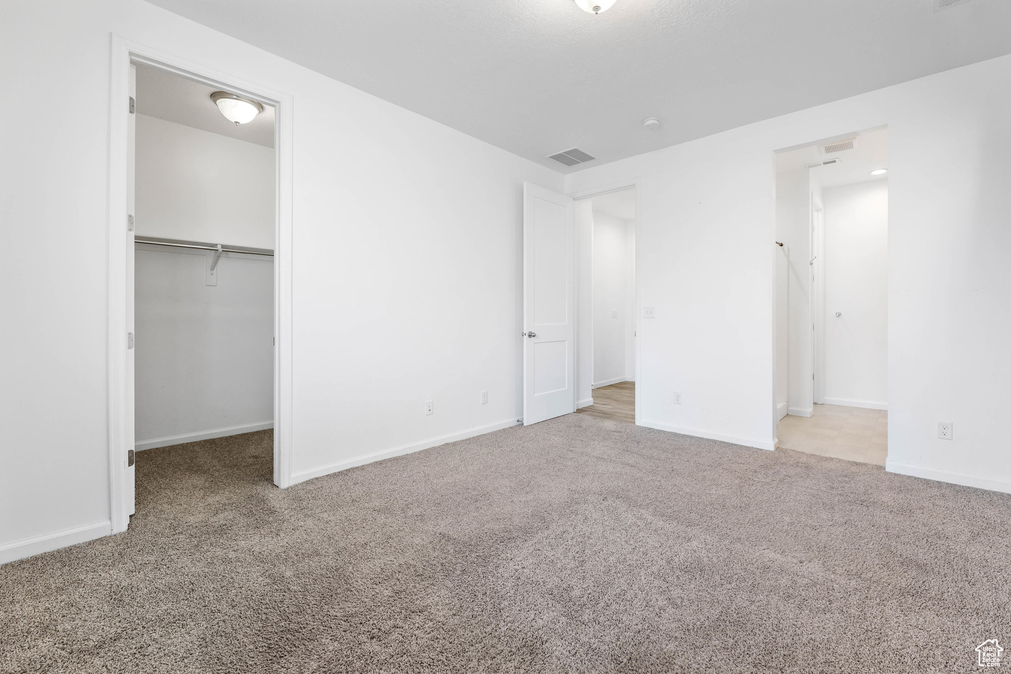 Unfurnished bedroom featuring a spacious closet, light colored carpet, and a closet