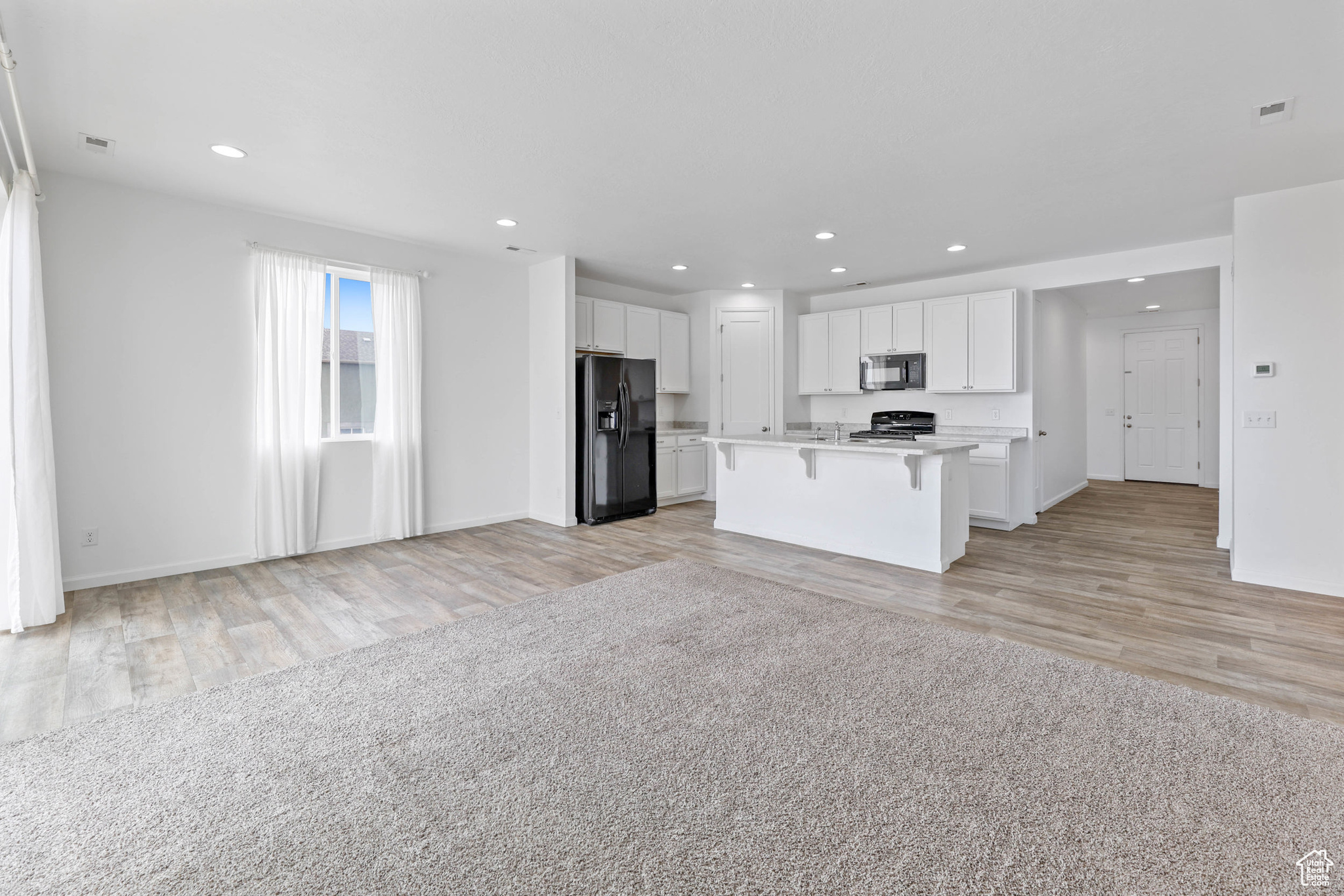 View of kitchen featuring white cabinets, a kitchen island with sink, a breakfast bar area, and black appliances along with the dining room from the view point of. the living room