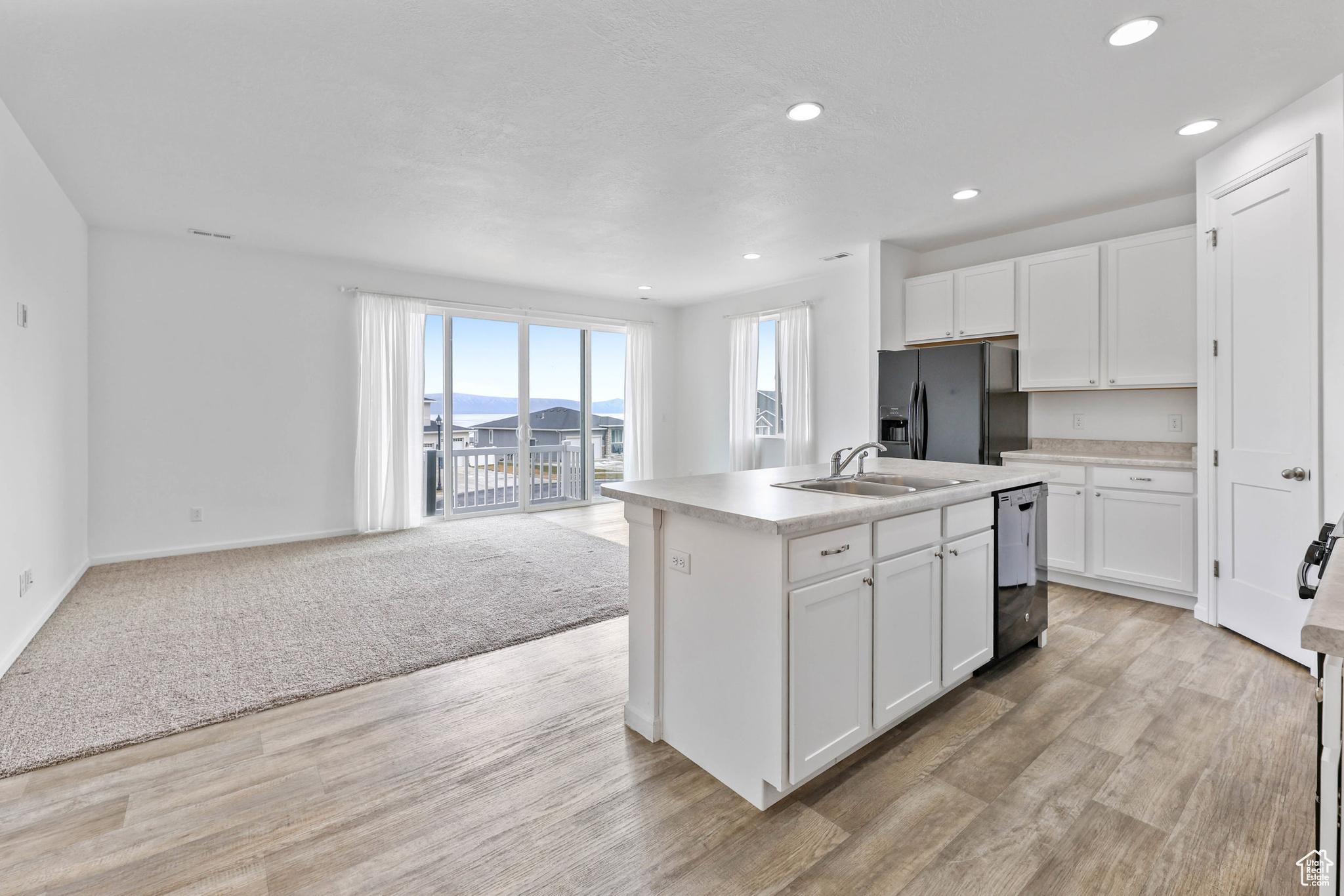 Kitchen featuring sink, white cabinetry, a center island with sink, stainless steel dishwasher, and black fridge