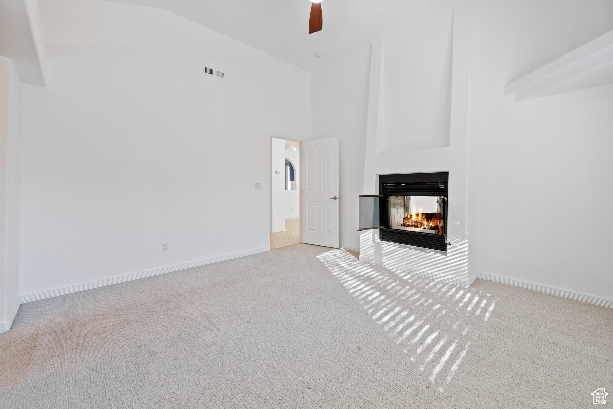 Unfurnished living room with a multi sided fireplace, light colored carpet, ceiling fan, and high vaulted ceiling