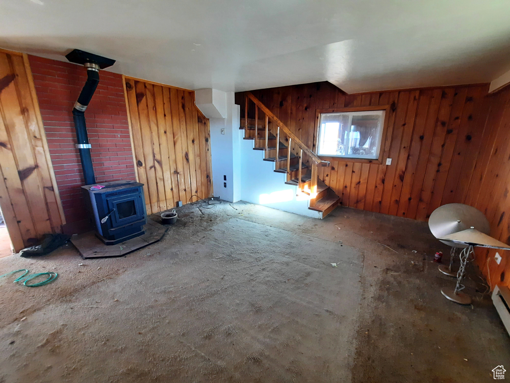 Unfurnished living room with a baseboard heating unit, a wood stove, and wood walls