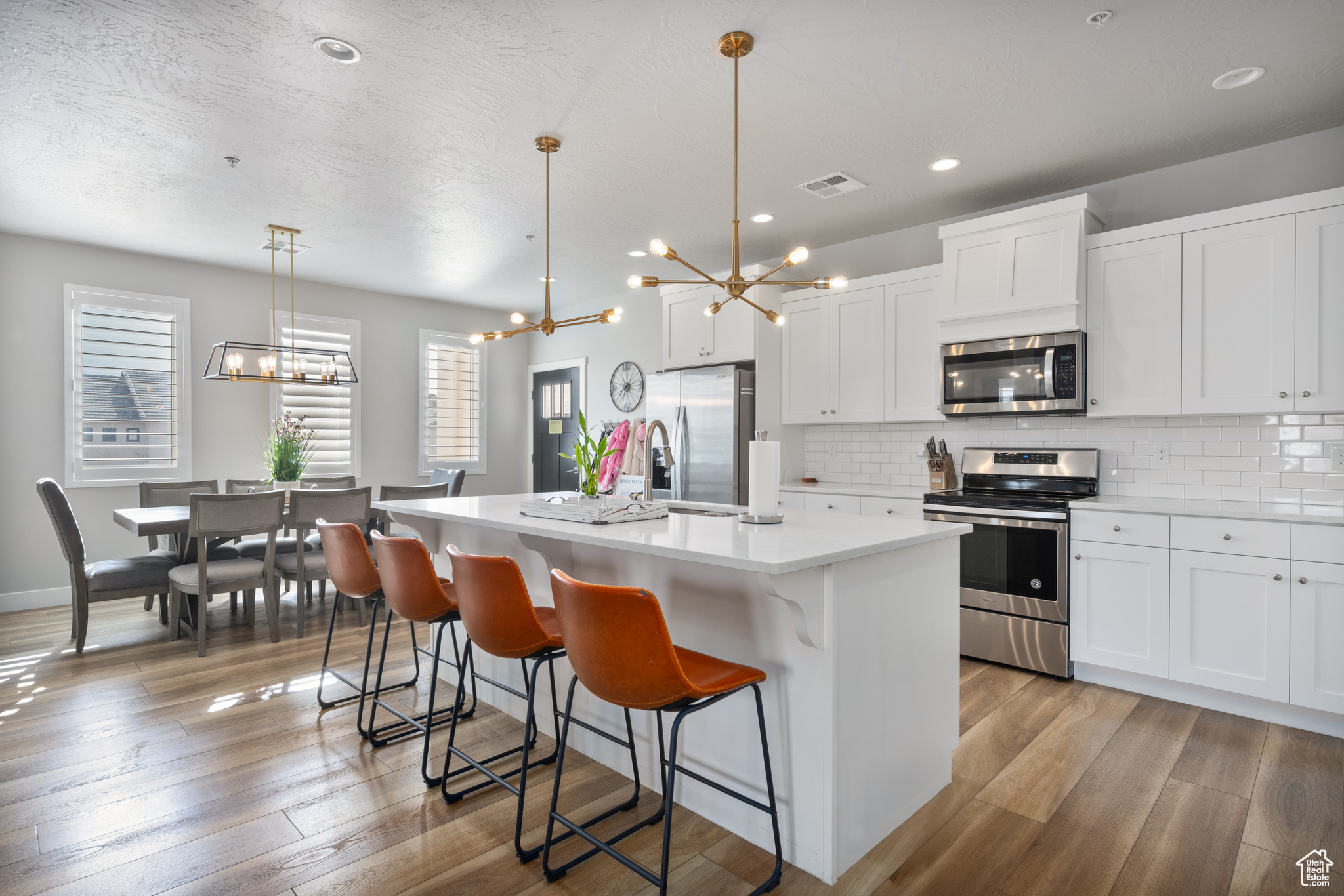 Kitchen with stainless steel appliances, hanging light fixtures, a kitchen island with sink, and white cabinets