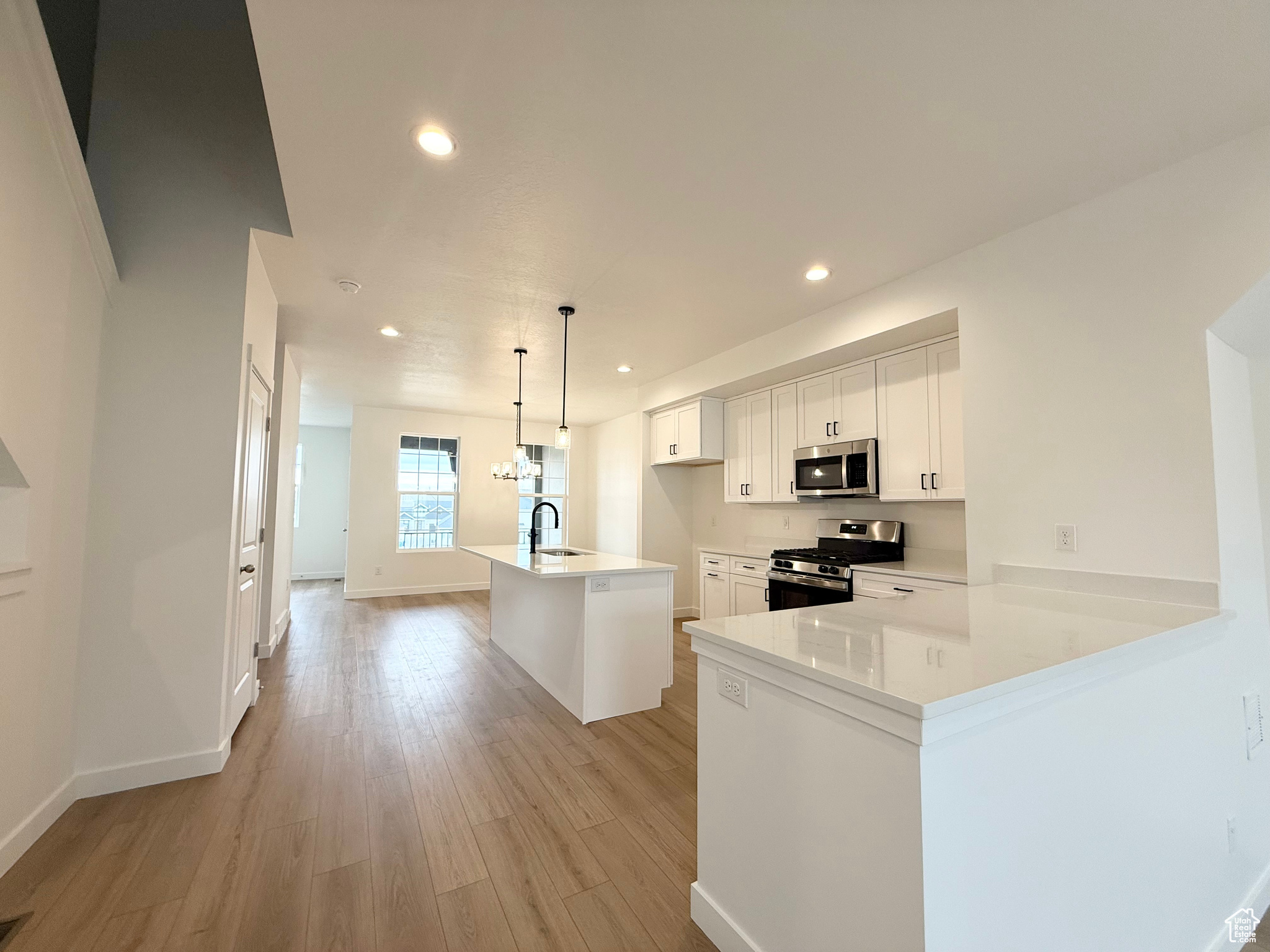 Kitchen featuring sink, white cabinetry, hanging light fixtures, stainless steel appliances, and kitchen peninsula