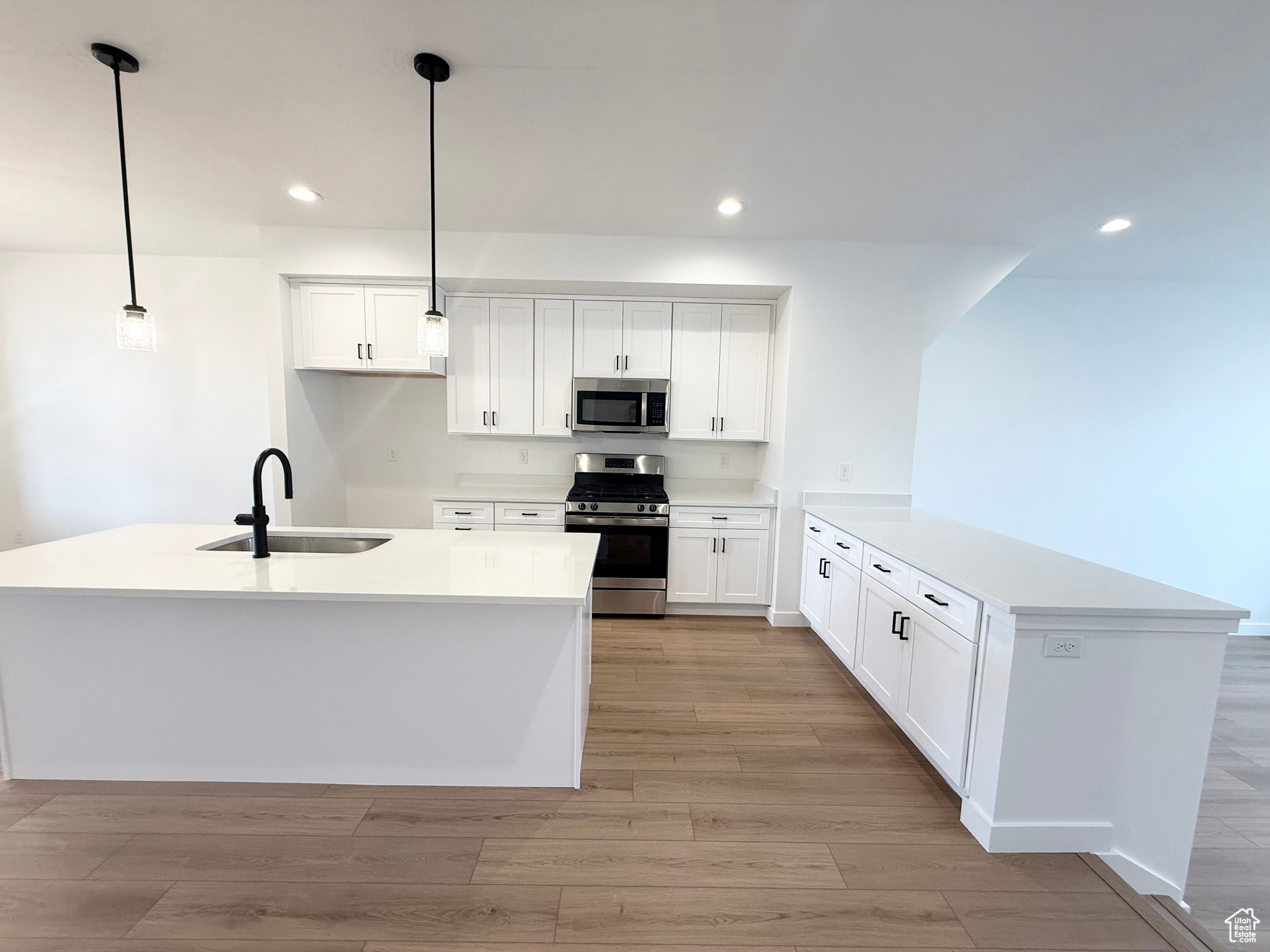 Kitchen with decorative light fixtures, a center island with sink, white cabinets, and appliances with stainless steel finishes