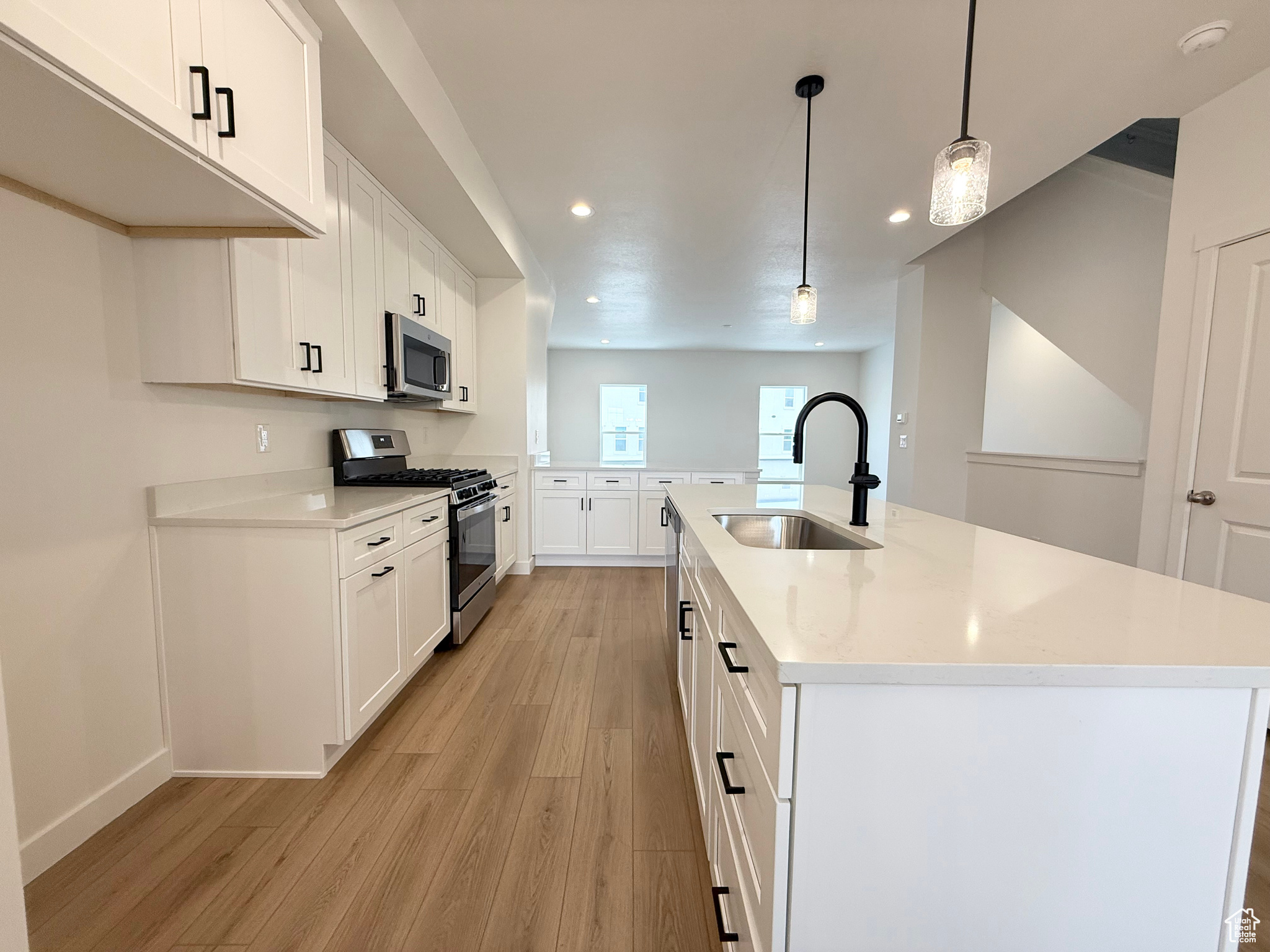 Kitchen featuring white cabinetry, stainless steel appliances, decorative light fixtures, and sink