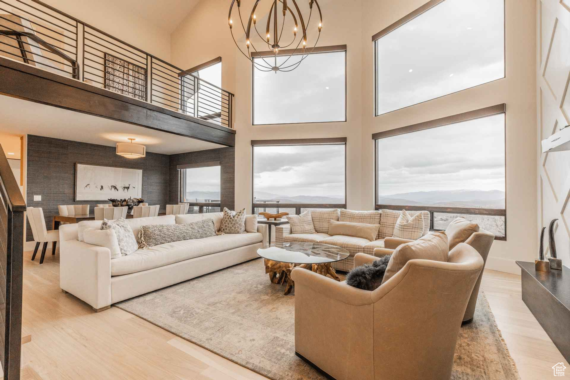 Living room with a high ceiling, plenty of natural light, an inviting chandelier, and light wood-type flooring