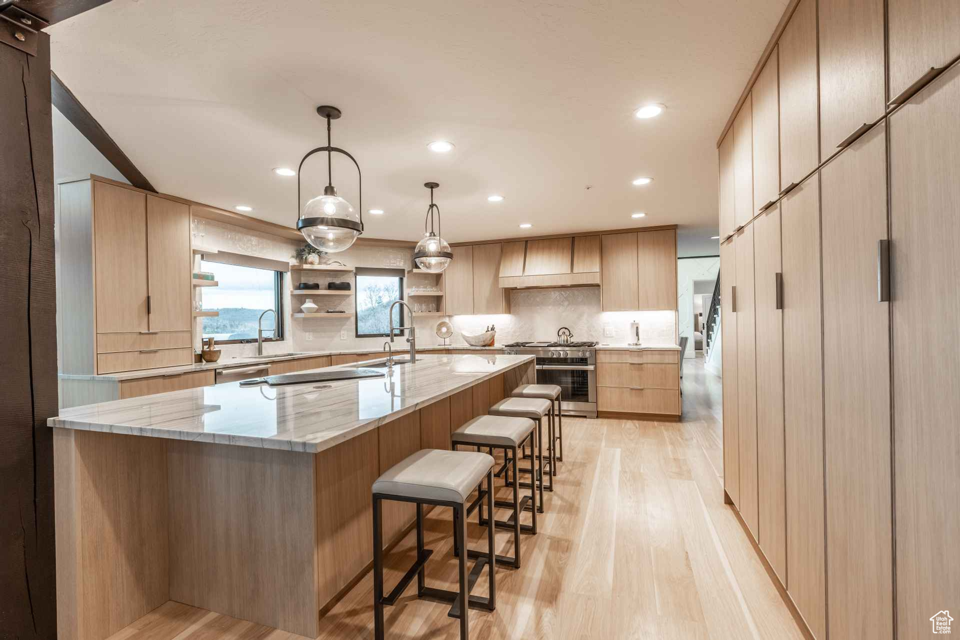 Kitchen featuring hanging light fixtures, a spacious island, tasteful backsplash, light stone countertops, and light brown cabinetry