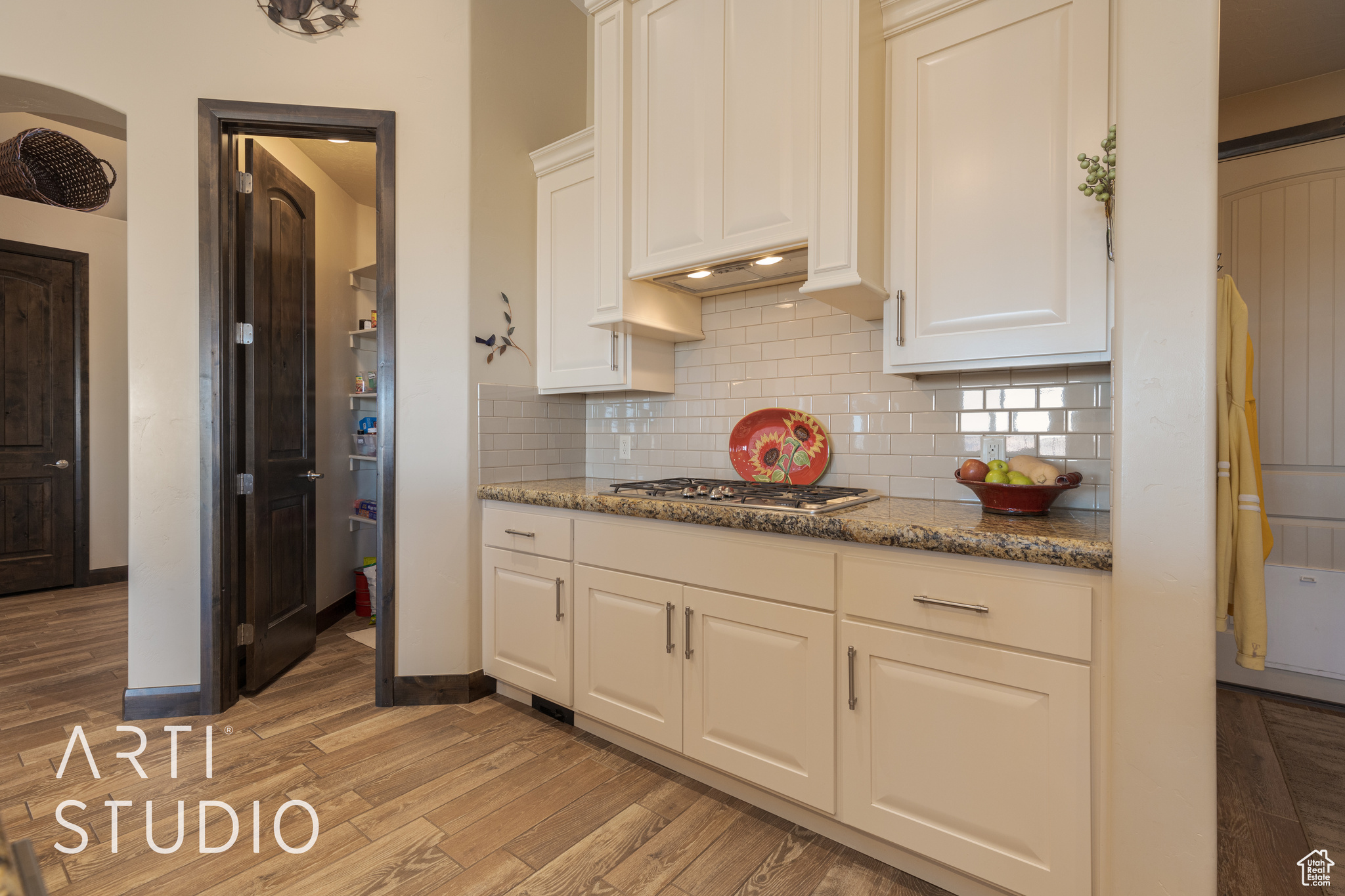 Kitchen with white cabinetry, stainless steel gas stovetop, wood look tile floors, and granite counters