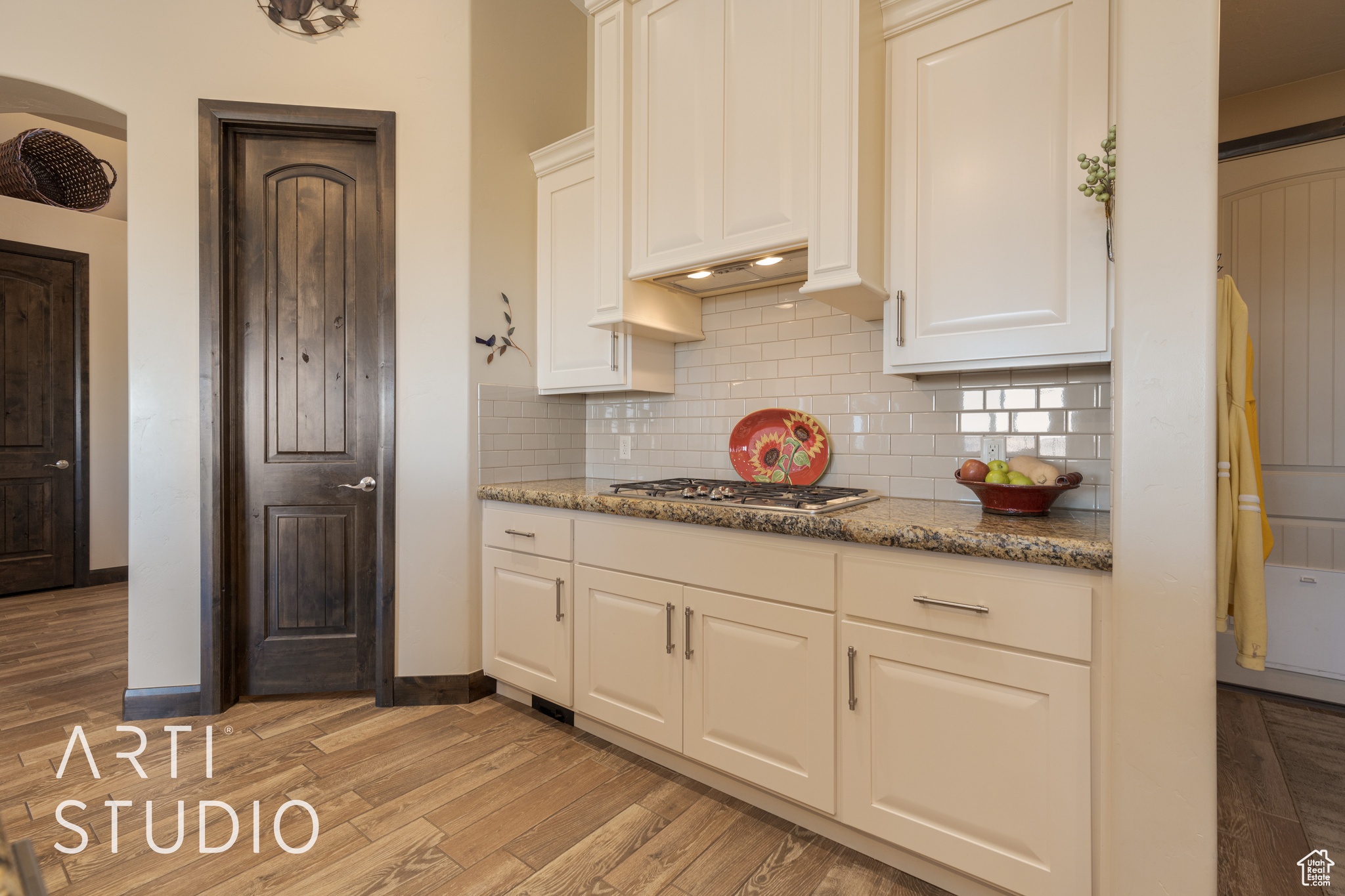 Kitchen with stainless steel gas stovetop, hood and white cabinetry, tasteful backsplash, light wood look tile flooring, and granite countertops and a side pantry