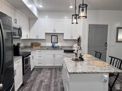 Kitchen featuring a kitchen bar, sink, decorative light fixtures, stainless steel appliances, and white cabinets