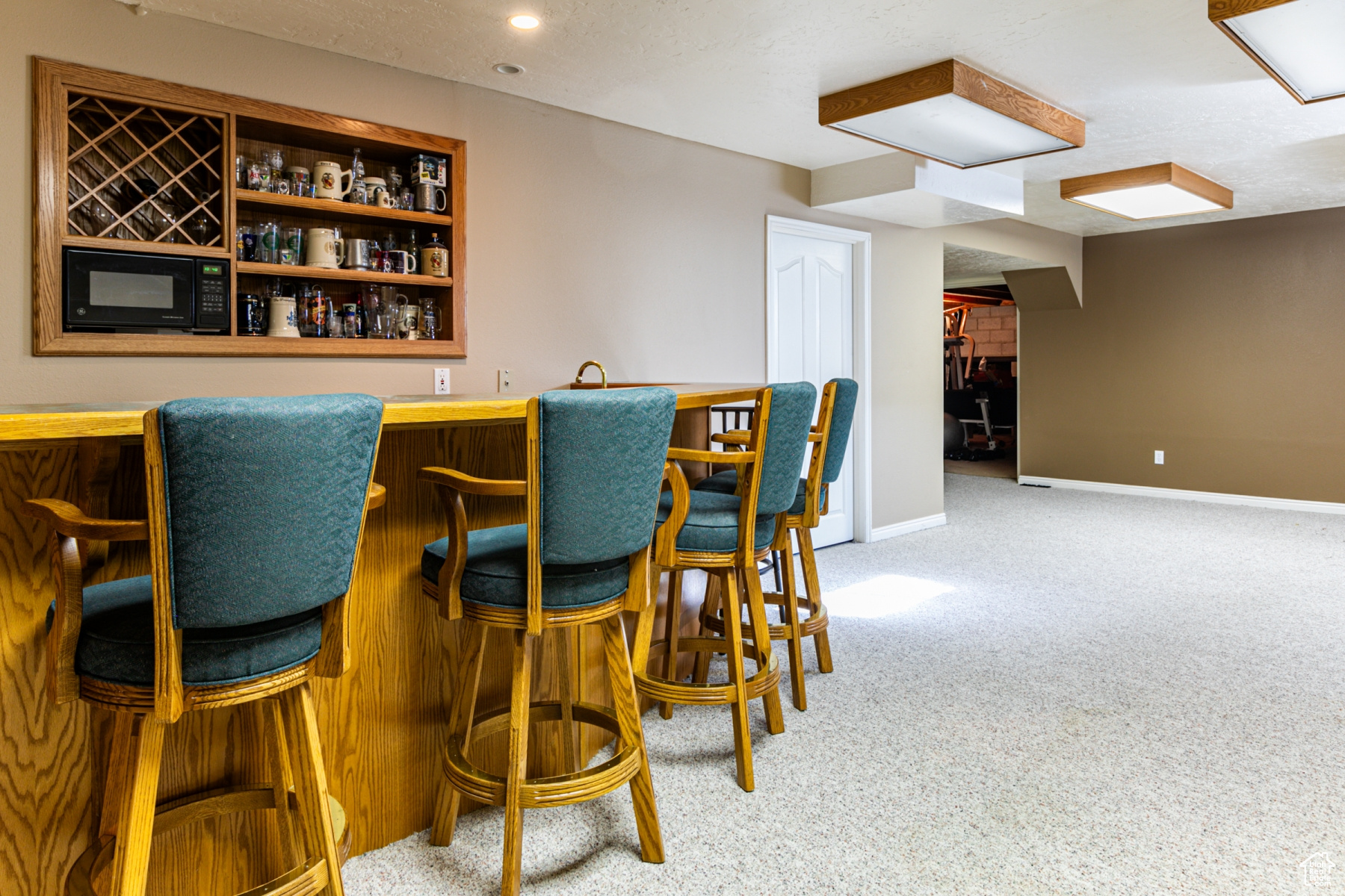 Bar featuring carpet floors, black microwave, and a textured ceiling