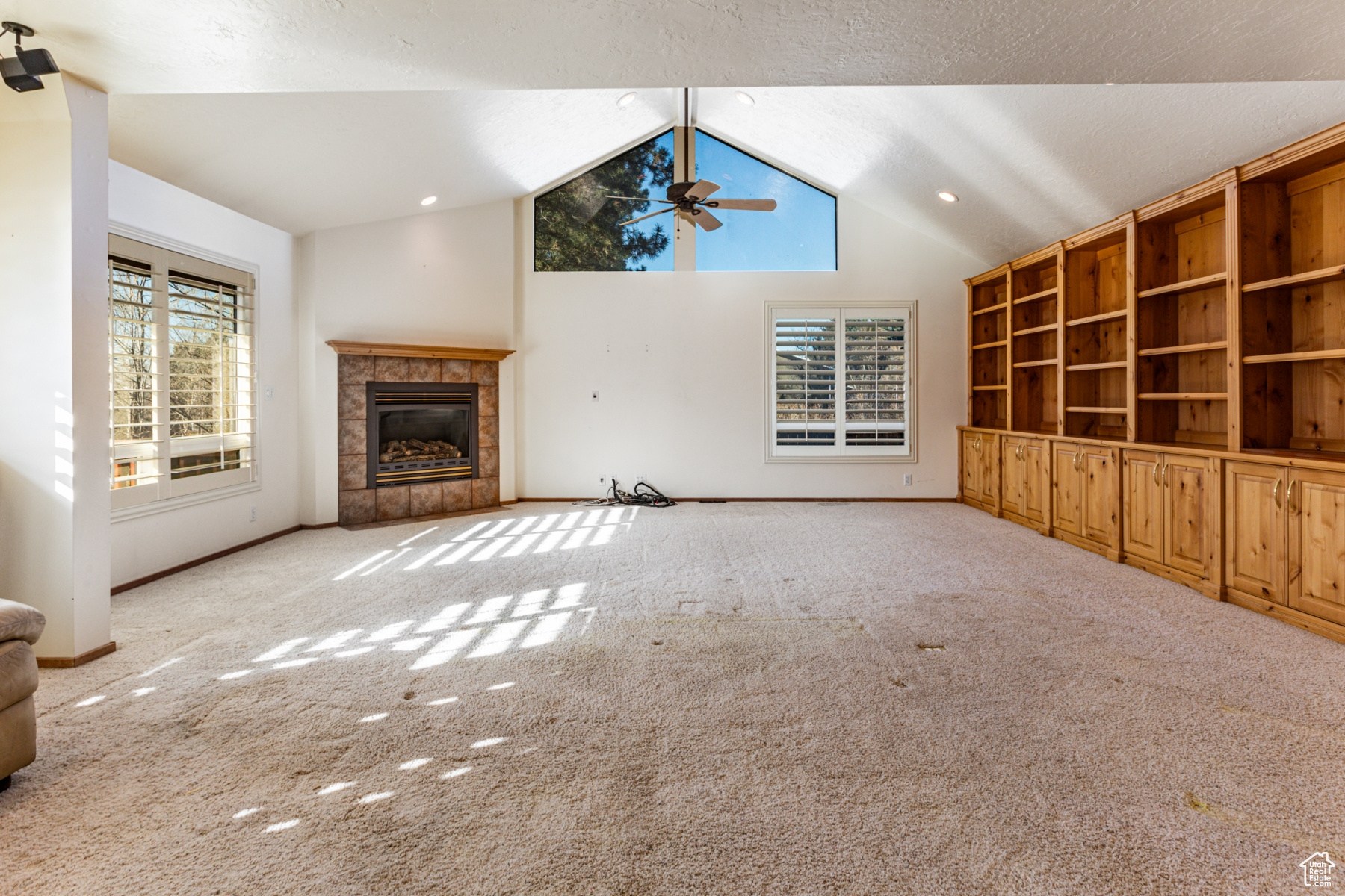 Unfurnished living room with light colored carpet, high vaulted ceiling, a textured ceiling, ceiling fan, and a tiled fireplace