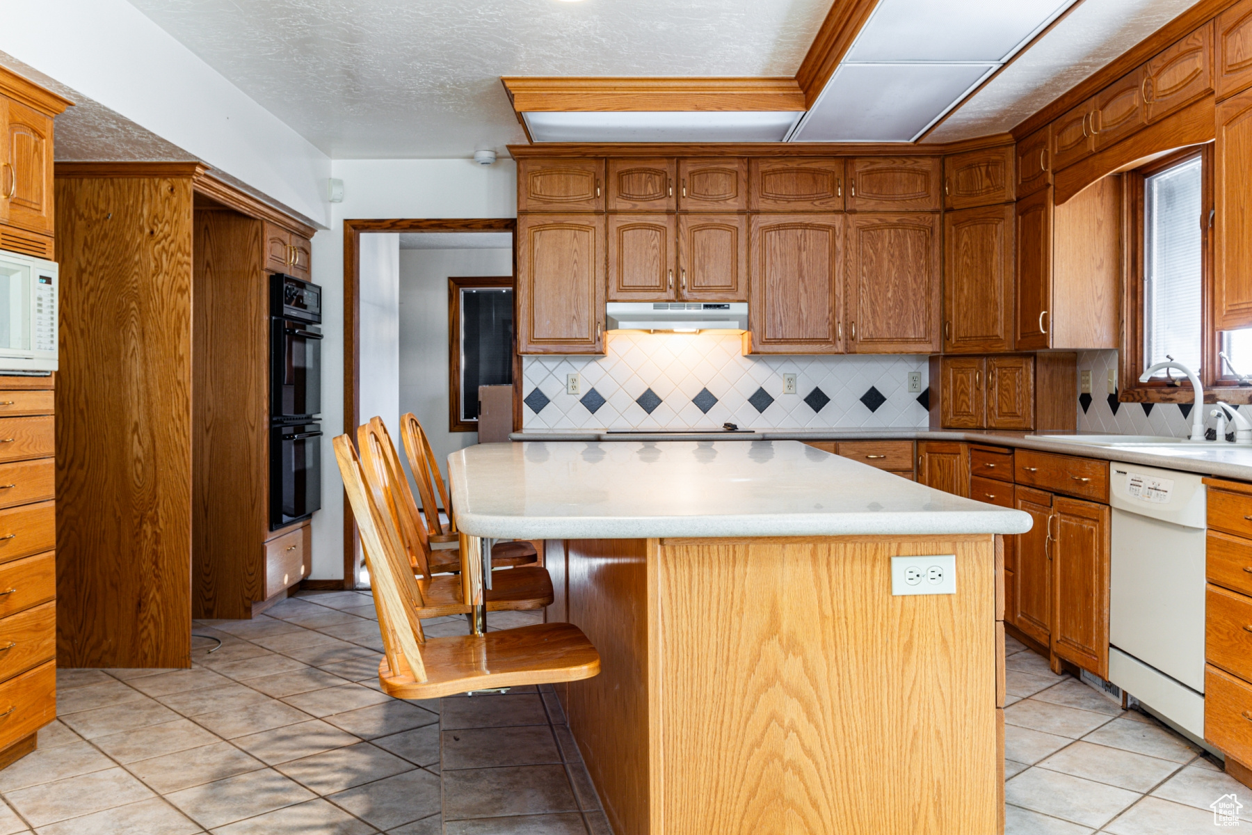 Kitchen featuring a kitchen island, sink, backsplash, a kitchen bar, and white appliances