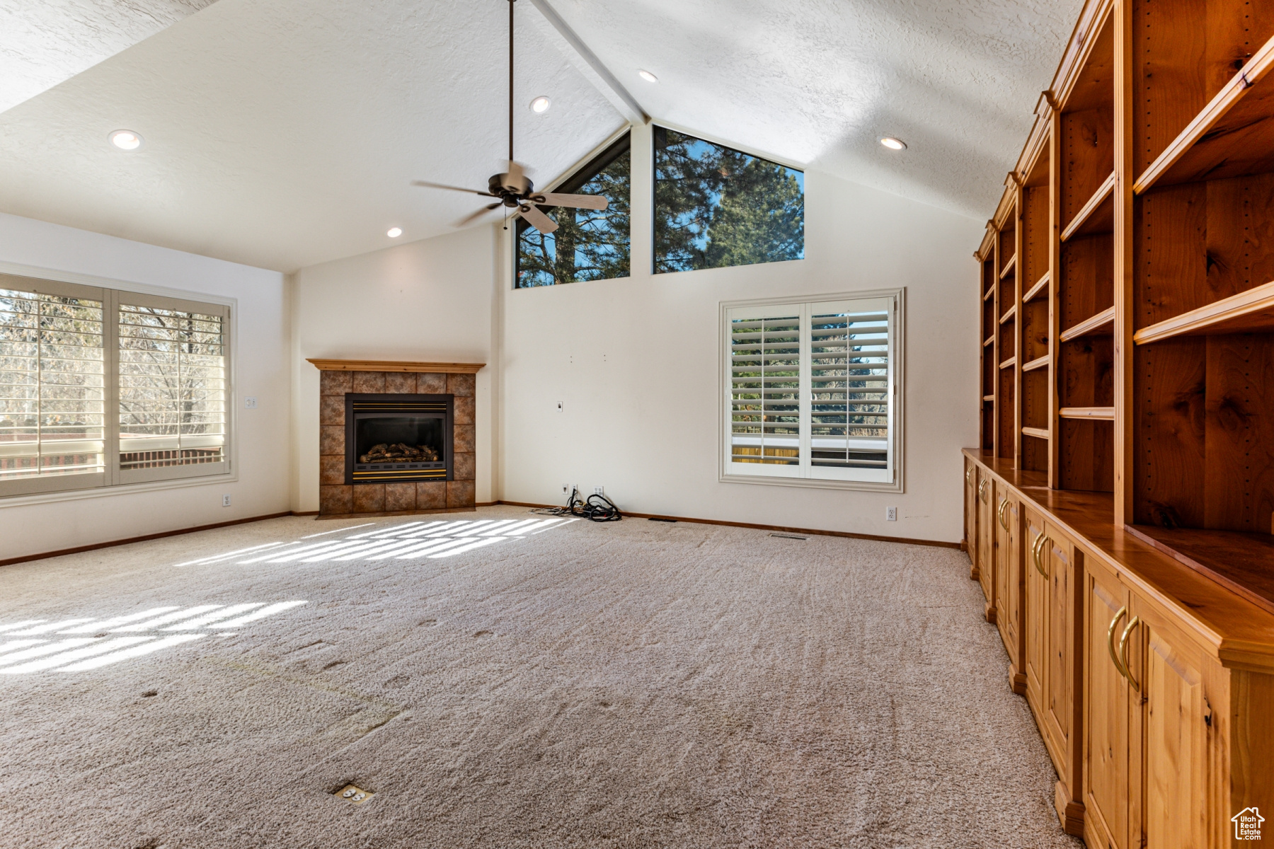 Unfurnished living room with light colored carpet, high vaulted ceiling, a textured ceiling, ceiling fan, and a fireplace