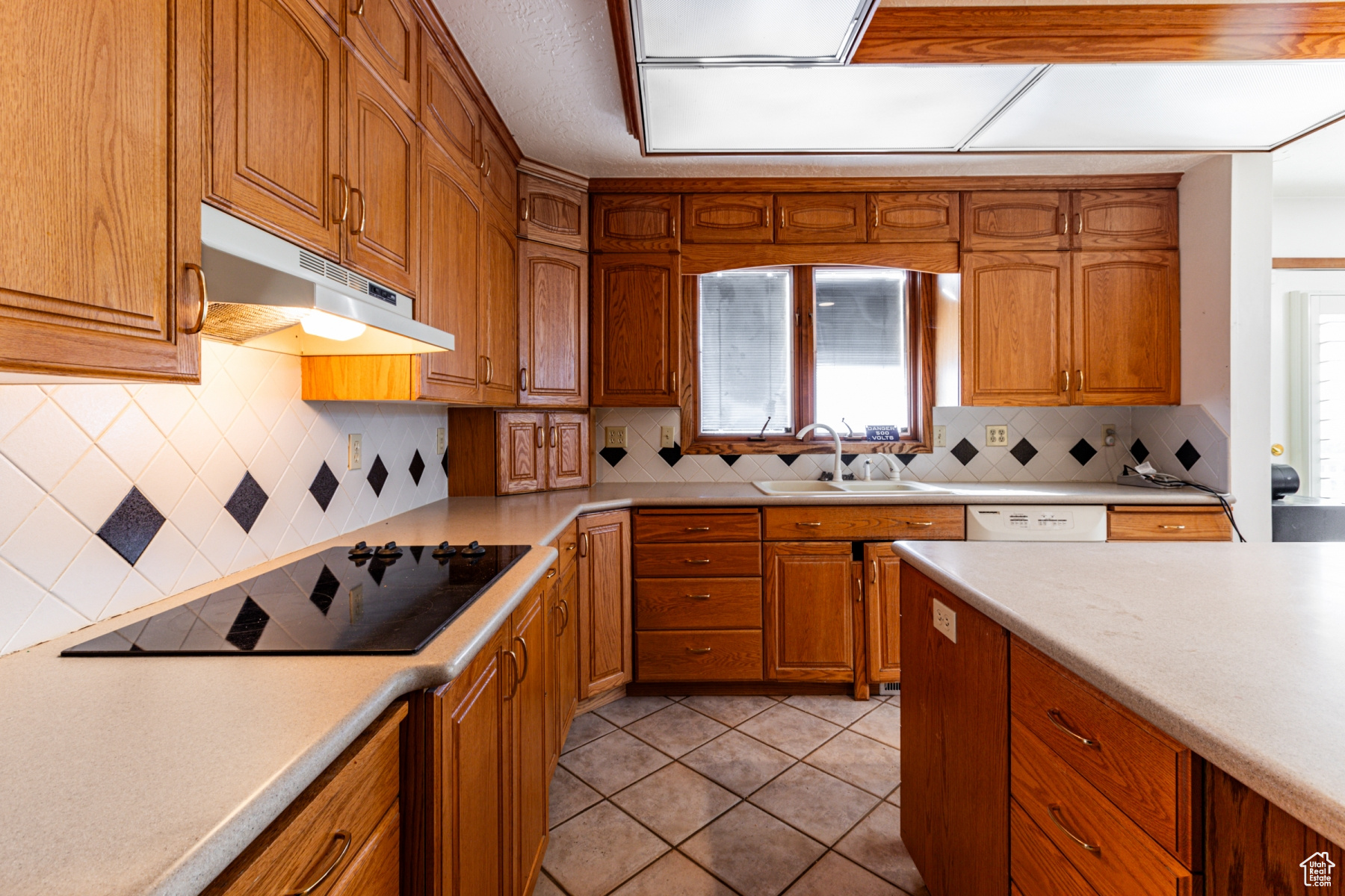 Kitchen with sink, decorative backsplash, black electric stovetop, light tile patterned floors, and white dishwasher