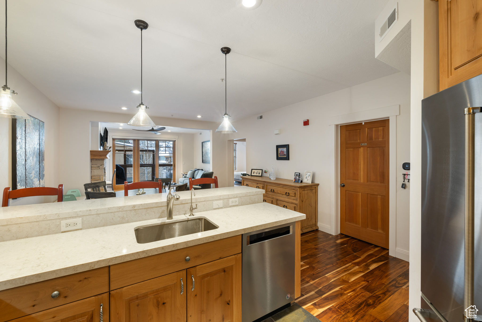 Kitchen featuring light stone counters, sink, hanging light fixtures, and appliances with stainless steel finishes