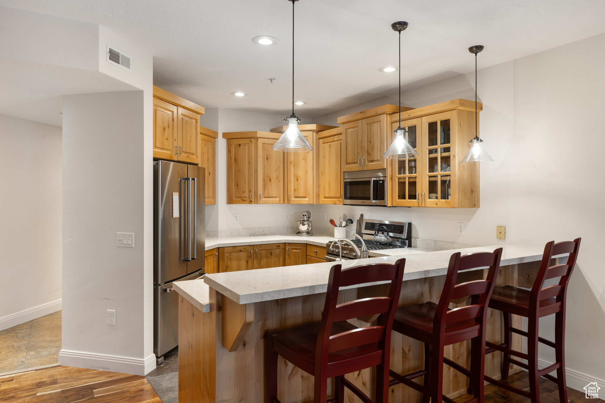 Kitchen with a breakfast bar area, appliances with stainless steel finishes, dark hardwood / wood-style floors, decorative light fixtures, and kitchen peninsula