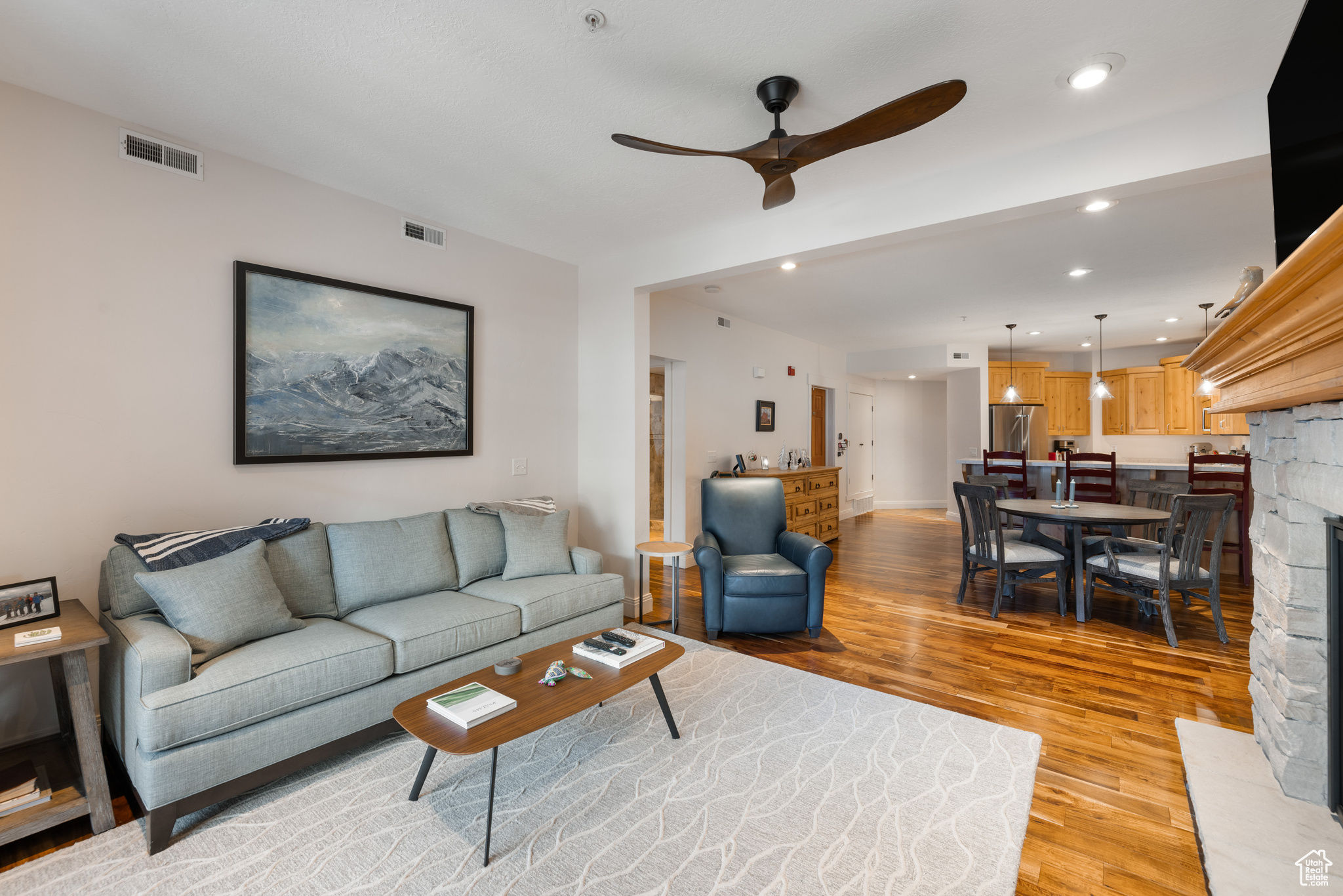 Living room with ceiling fan, a stone fireplace, and light hardwood / wood-style floors