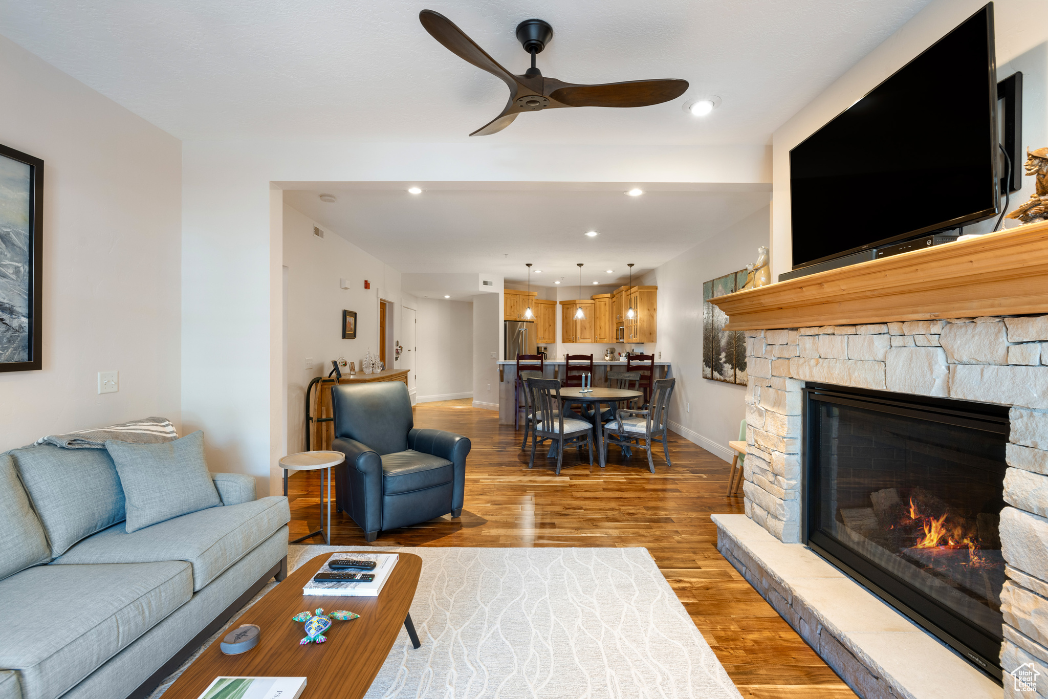 Living room featuring a stone fireplace, hardwood / wood-style floors, and ceiling fan