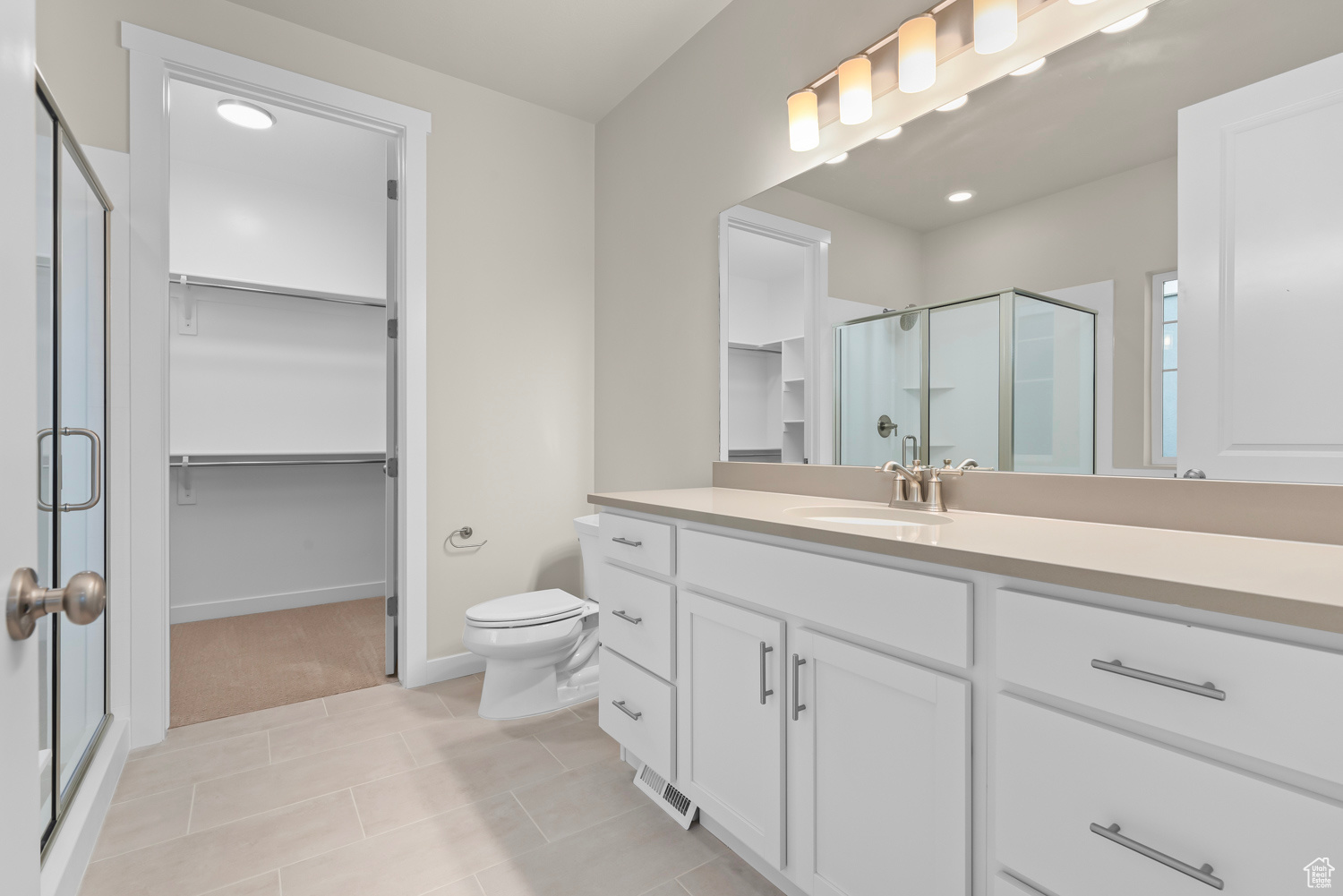 Bathroom featuring a shower with door, vanity, tile patterned floors, and toilet