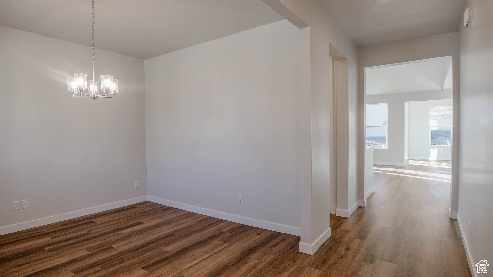 Unfurnished room featuring an inviting chandelier, baseboards, and wood finished floors