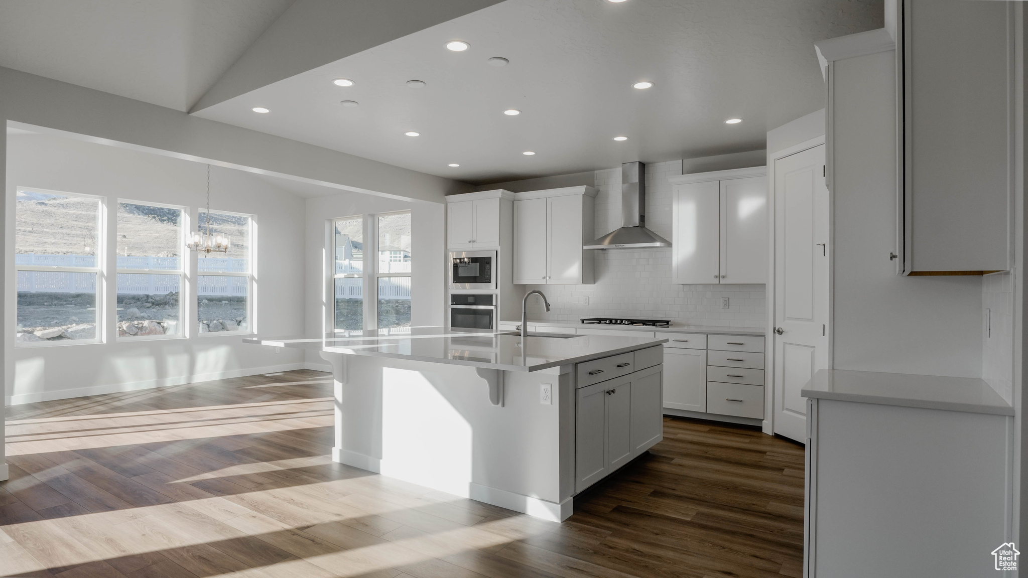 Kitchen with dark wood-style floors, built in microwave, oven, wall chimney exhaust hood, and backsplash