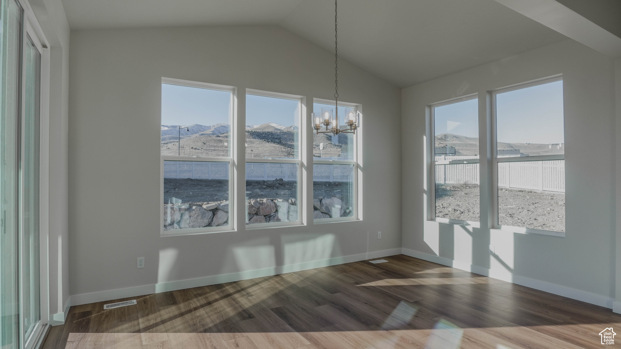 Unfurnished dining area featuring vaulted ceiling, wood finished floors, baseboards, and a chandelier