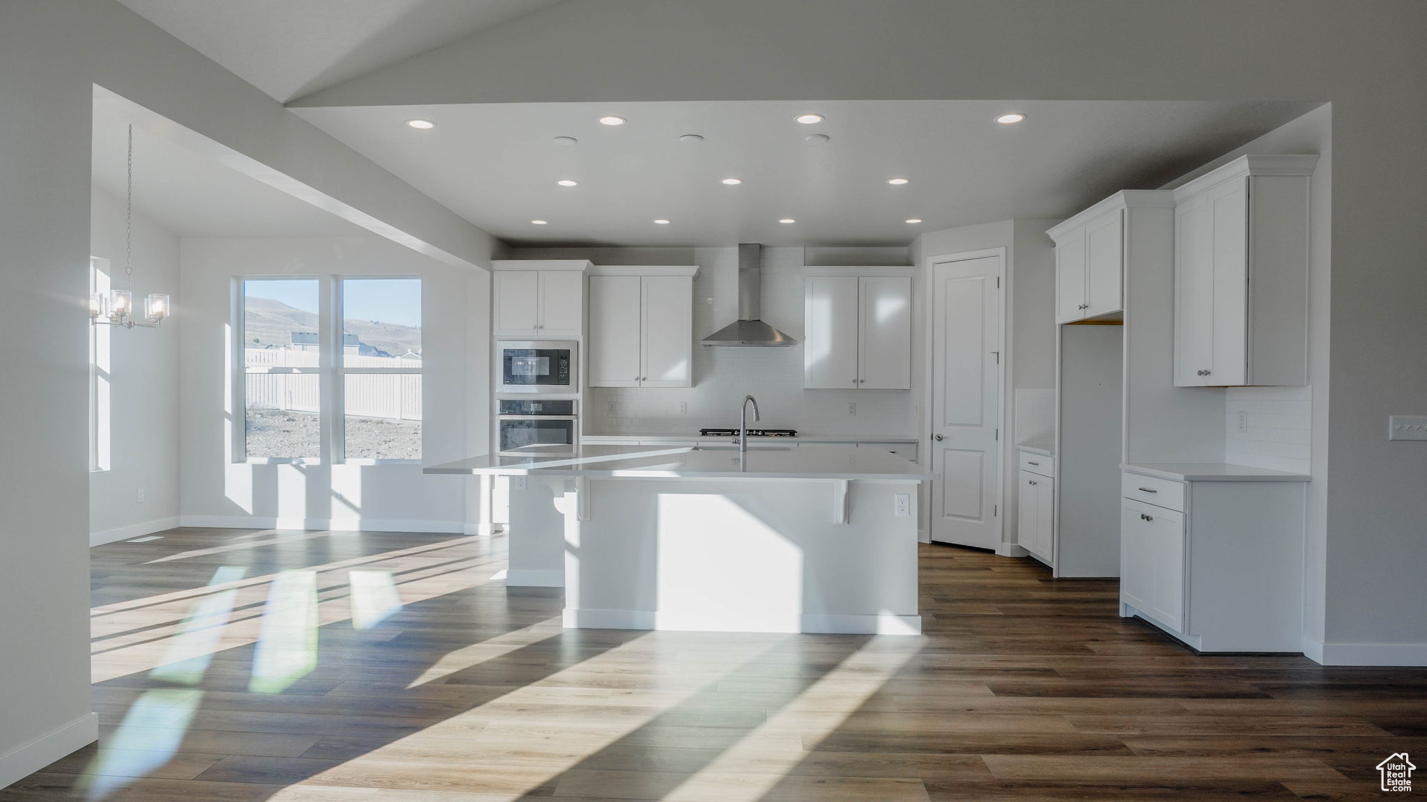Kitchen with dark wood-type flooring, oven, wall chimney range hood, built in microwave, and white cabinetry