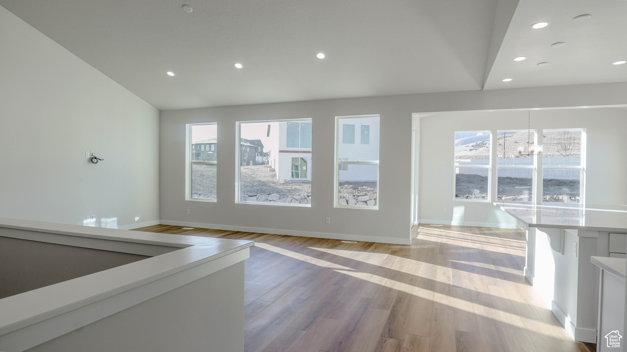 Unfurnished living room featuring baseboards, an inviting chandelier, light wood-style flooring, lofted ceiling, and recessed lighting