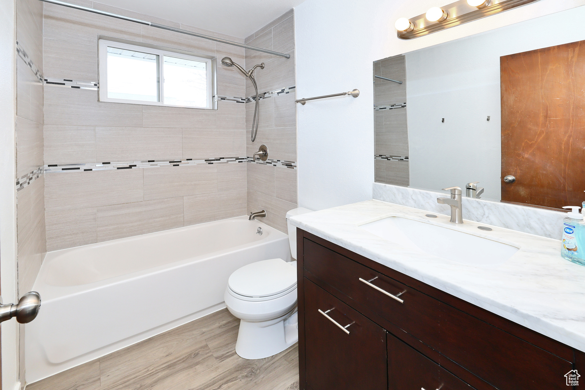 Full bathroom with tiled shower / bath combo, vanity, hardwood / wood-style floors, and toilet