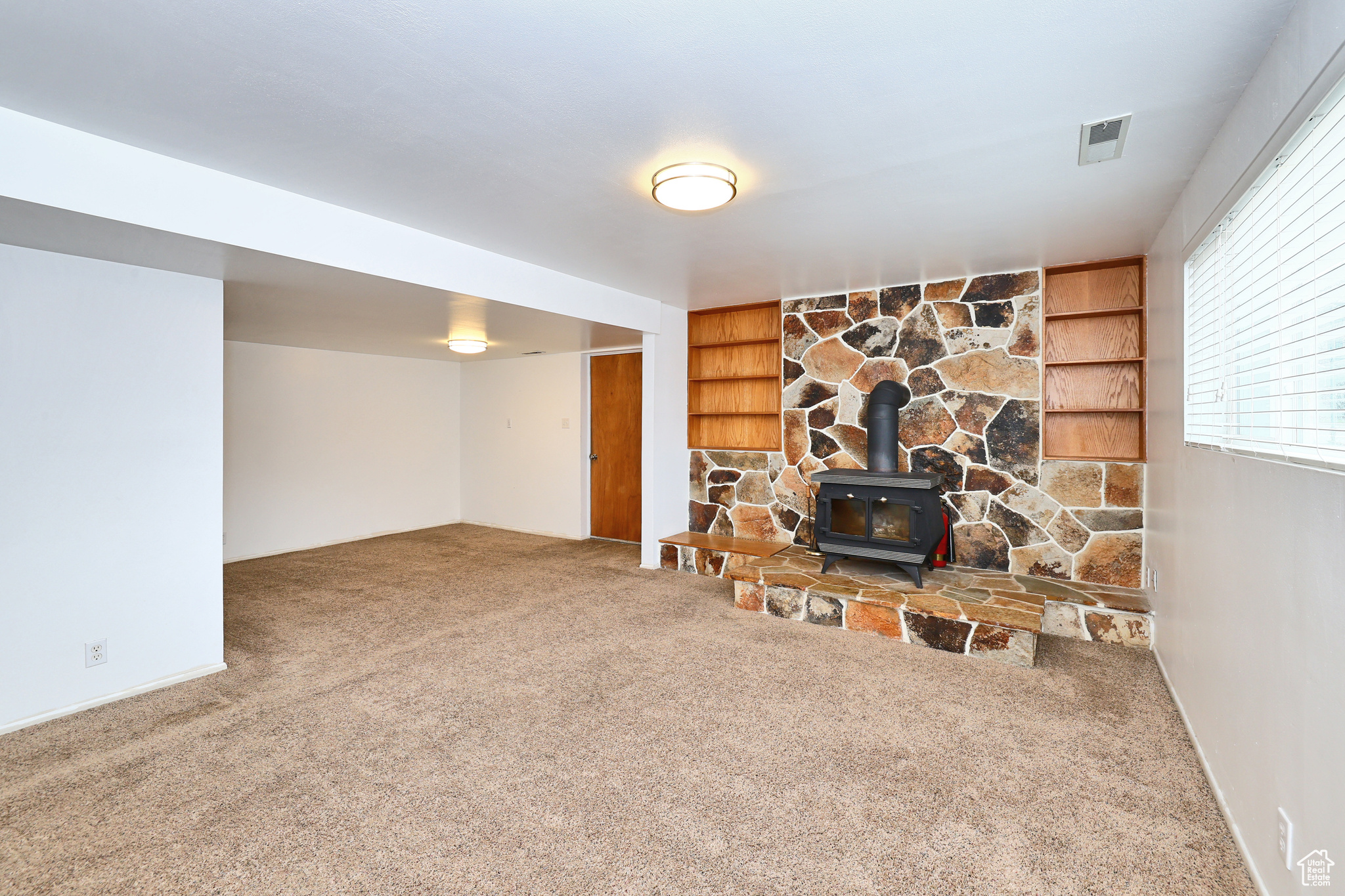 Living room featuring carpet floors, built in features, and a wood stove