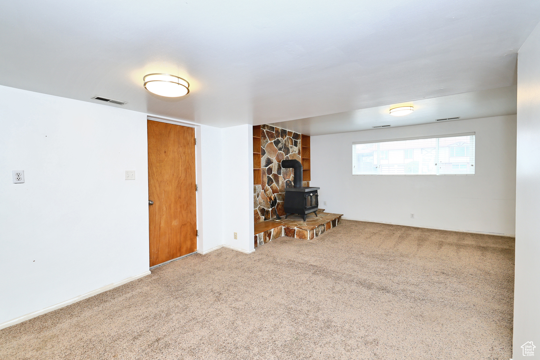 Unfurnished living room featuring carpet and a wood stove