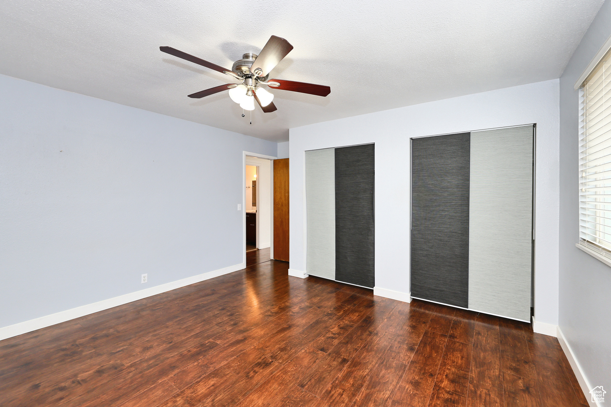 Unfurnished bedroom featuring multiple closets, ceiling fan, dark wood-type flooring, and multiple windows