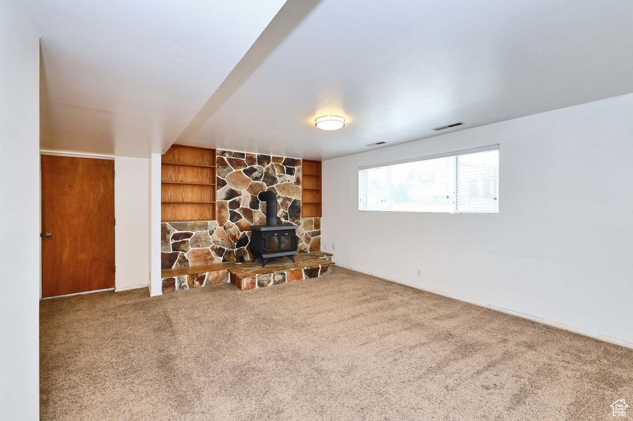 Unfurnished living room featuring carpet floors, built in features, and a wood stove