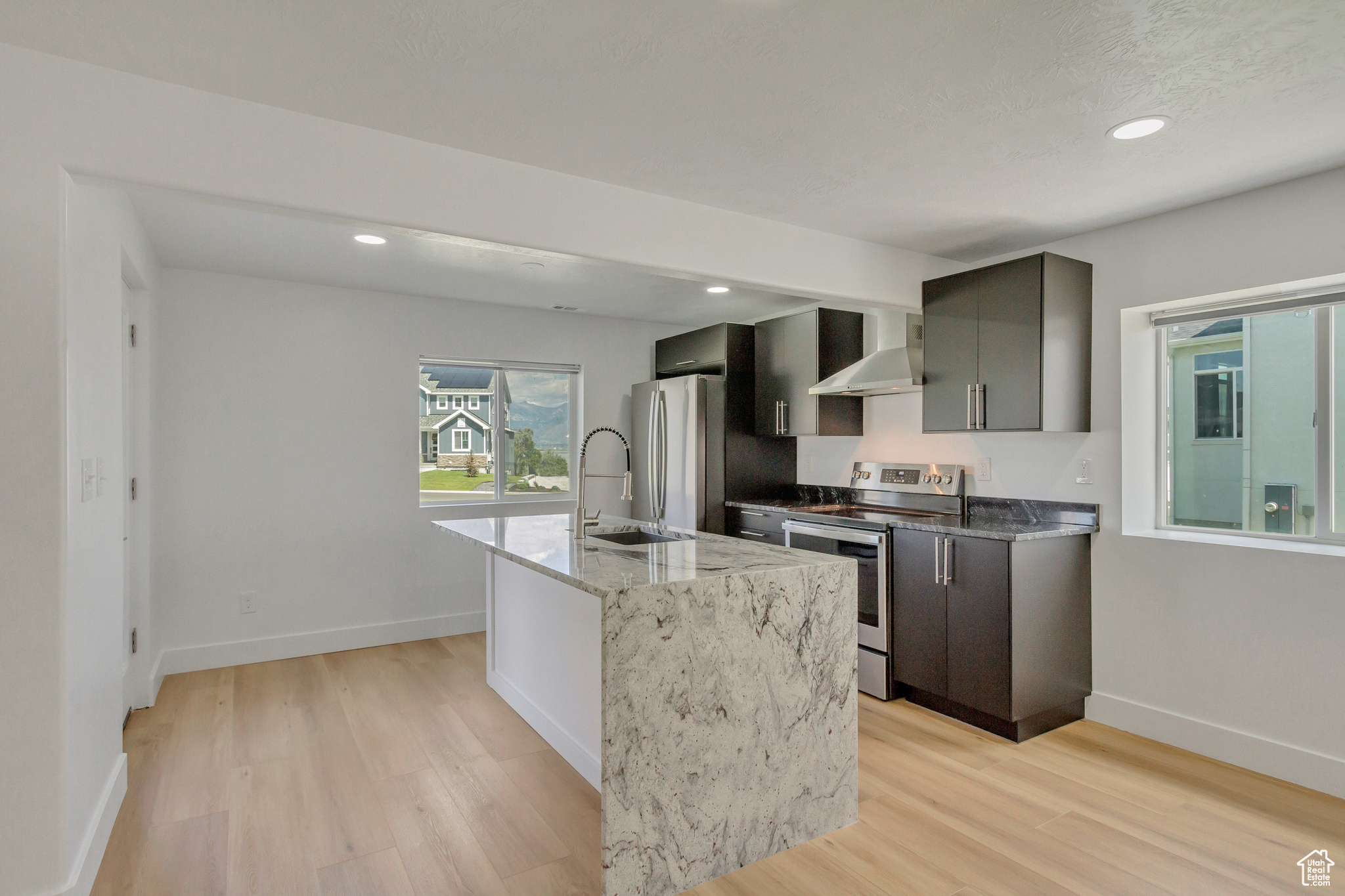 Kitchen with wall chimney exhaust hood, sink, a center island with sink, light wood-type flooring, and appliances with stainless steel finishes